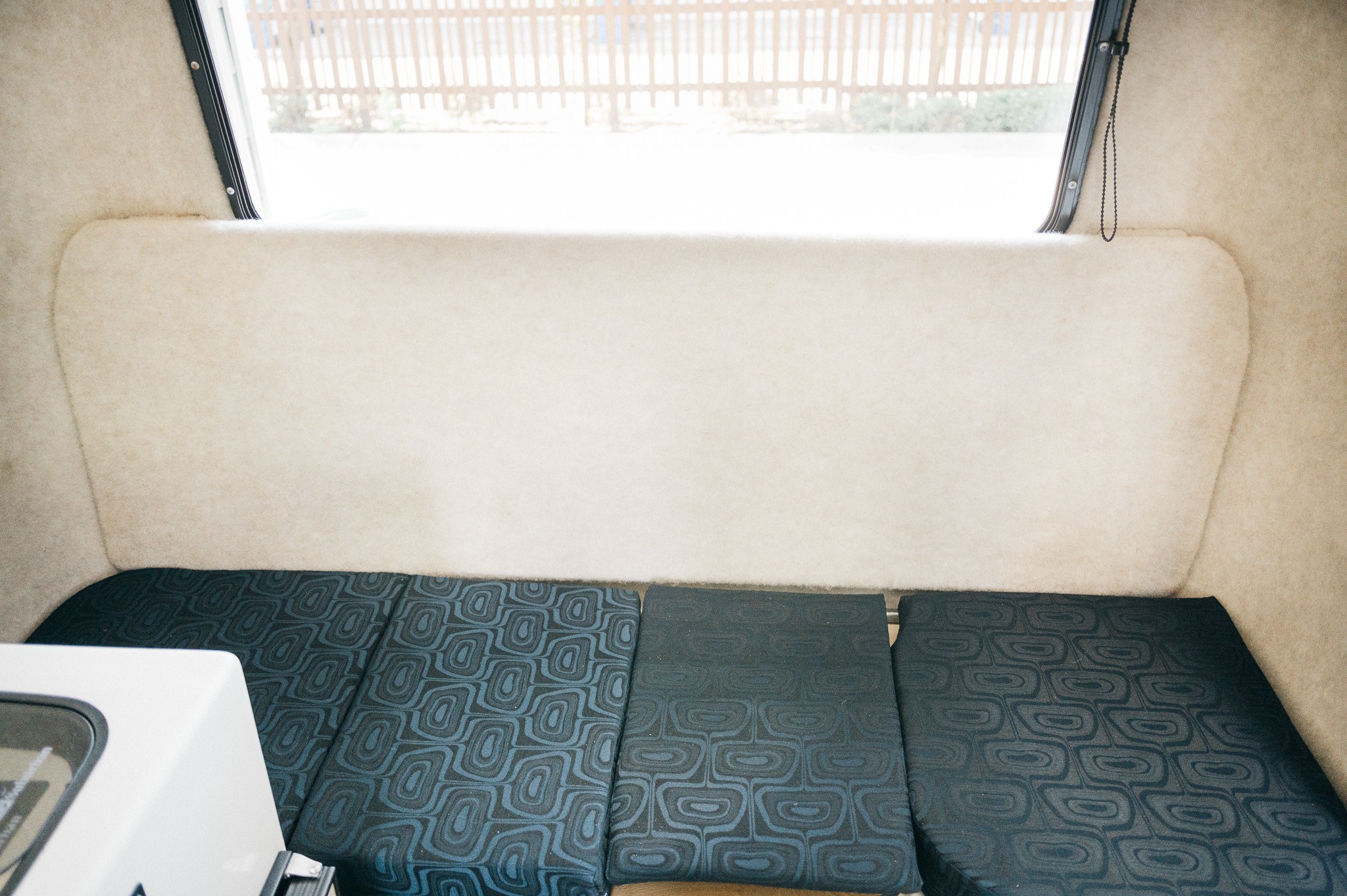 Cozy RV rental interior: cream-colored walls, dark patterned bed cushions, and a bright window overlooking a fence.. Outback Trailer Manufacturing the Outback 2017