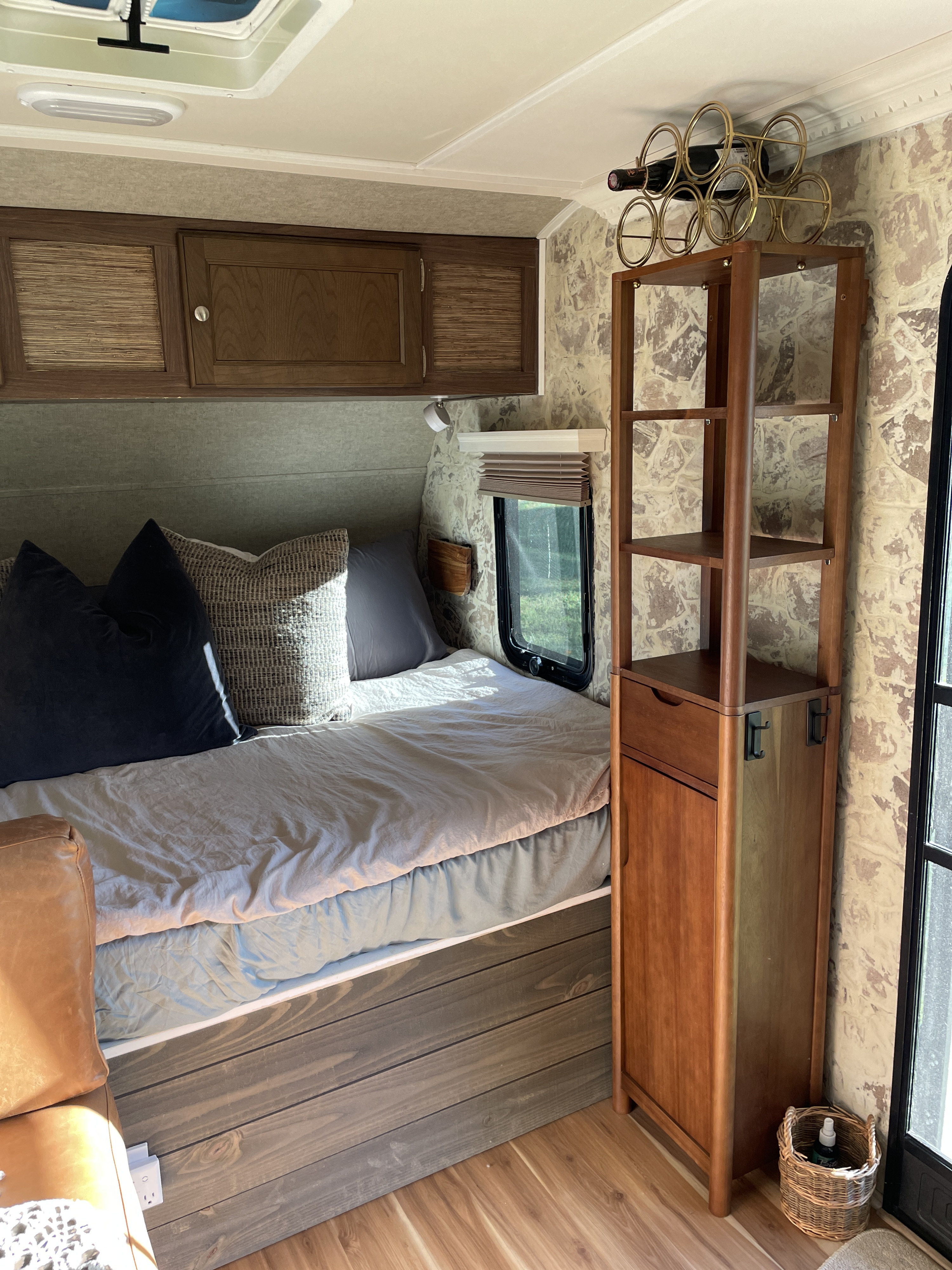 Cozy RV rental interior featuring a bed/daybed, overhead storage, and a tall shelving unit topped with a wine rack.. Forest River Palomino Palomini 2017