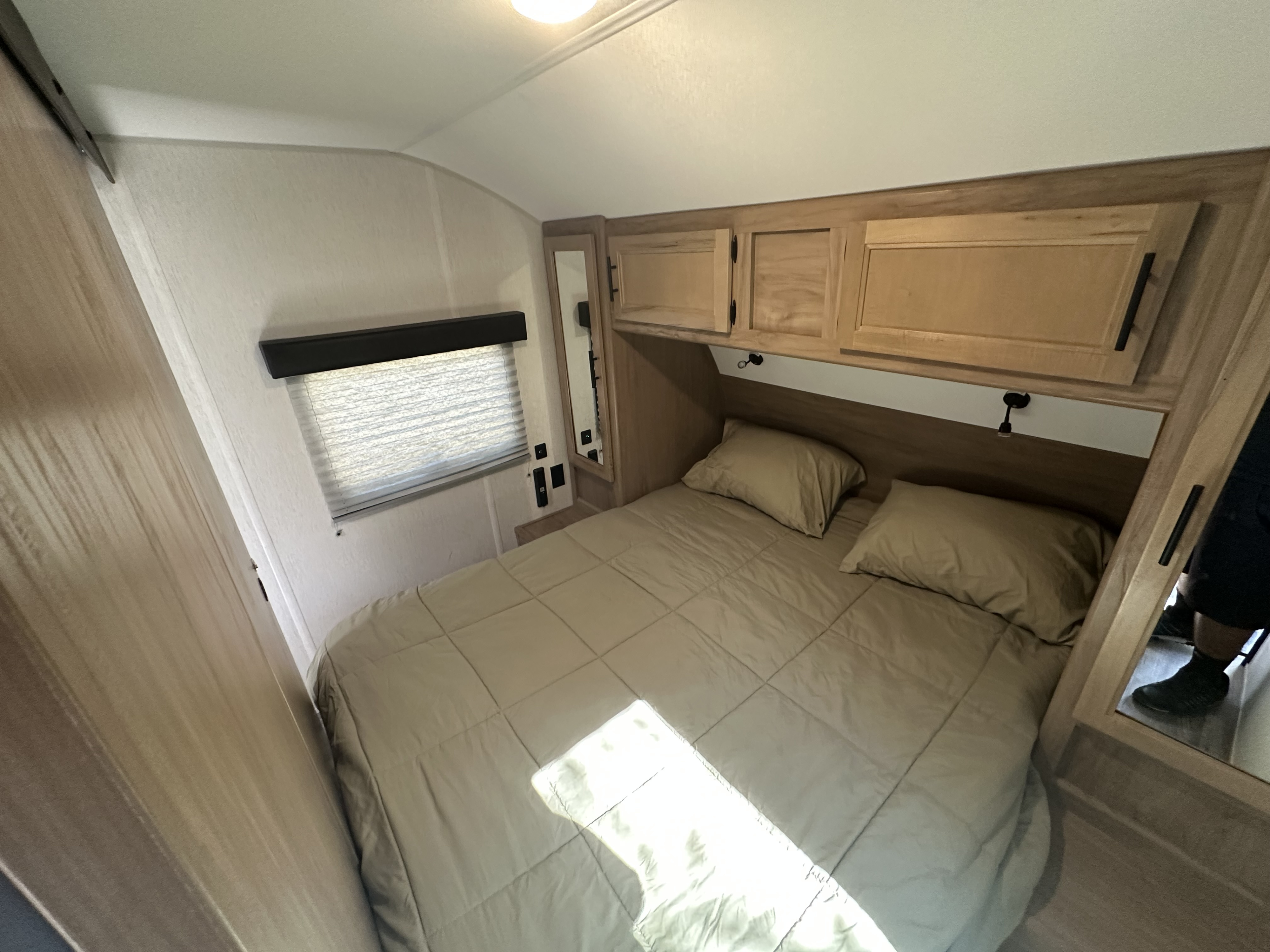 Cozy RV rental bedroom with a comfy bed, wood overhead cabinets, and a window with blinds. Ideal for travel.. Forest River Cherokee Grey Wolf Black Label 2023
