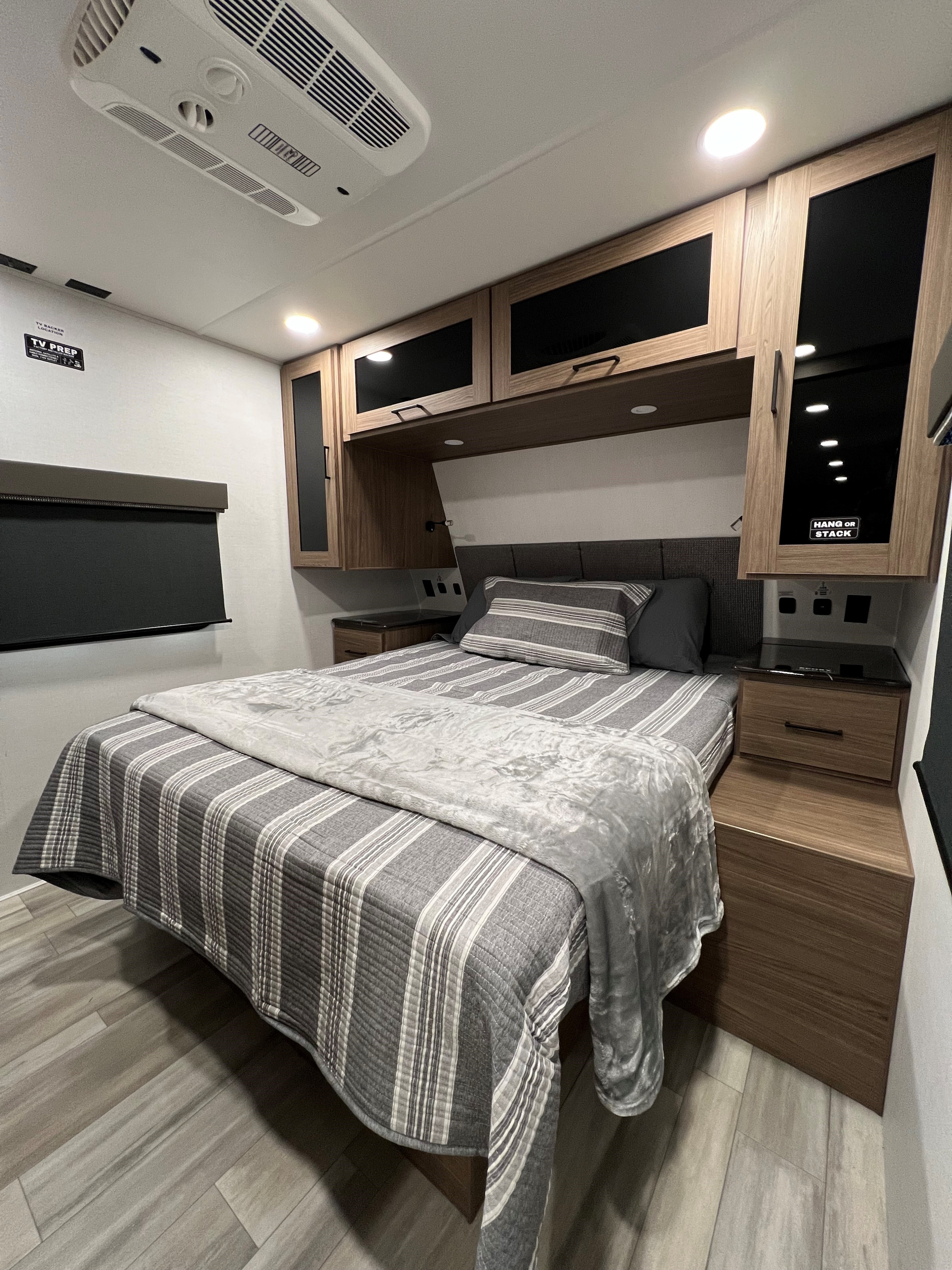 Cozy RV rental bedroom featuring a striped bed, overhead storage, nightstands, and integrated lighting & AC for comfort.. Alliance Delta 321 bh 2025