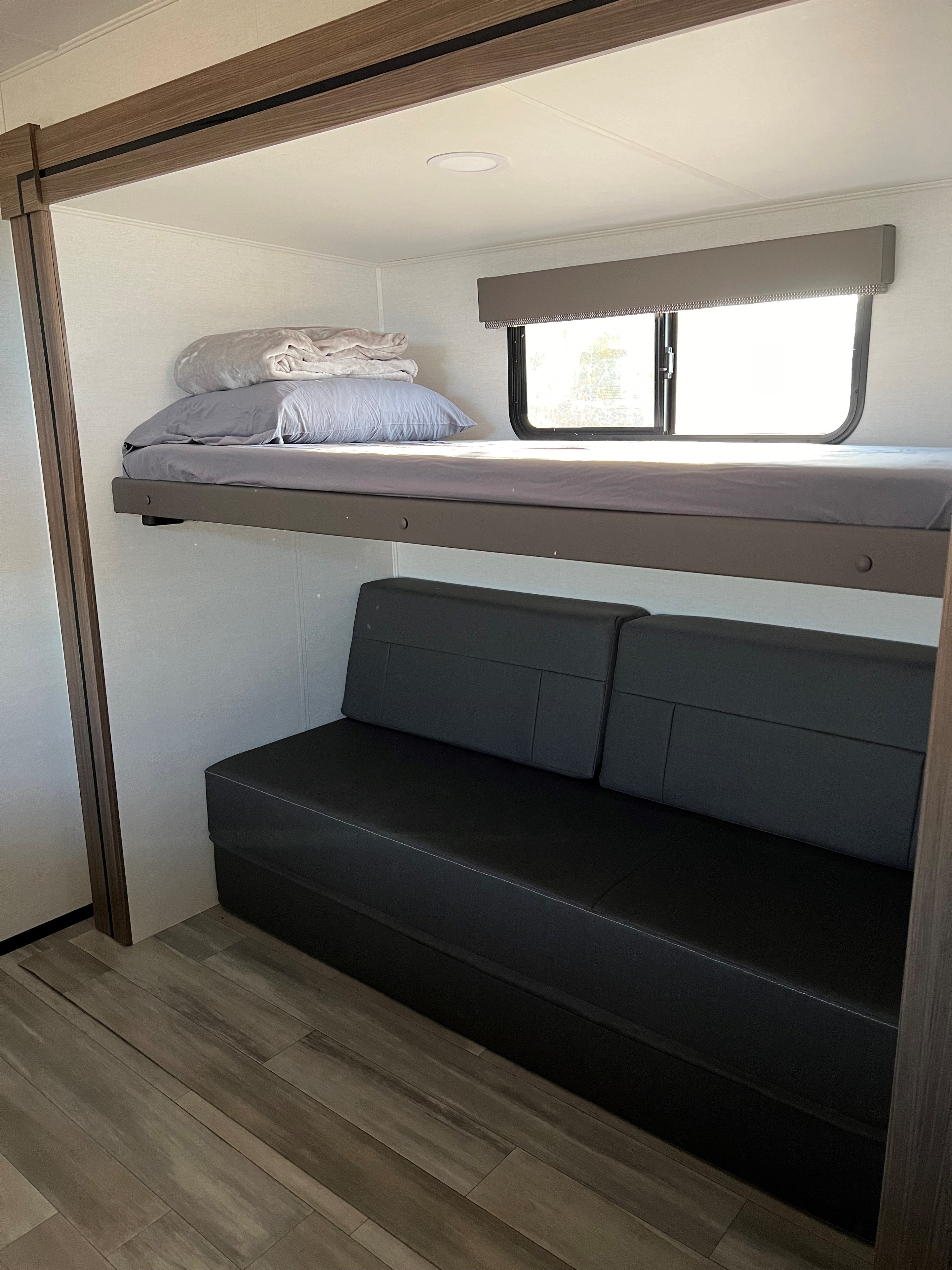 RV rental interior: a clean bunk bed with window above a dark sofa, offering cozy sleeping and seating space.. Alliance Delta 321 bh 2025