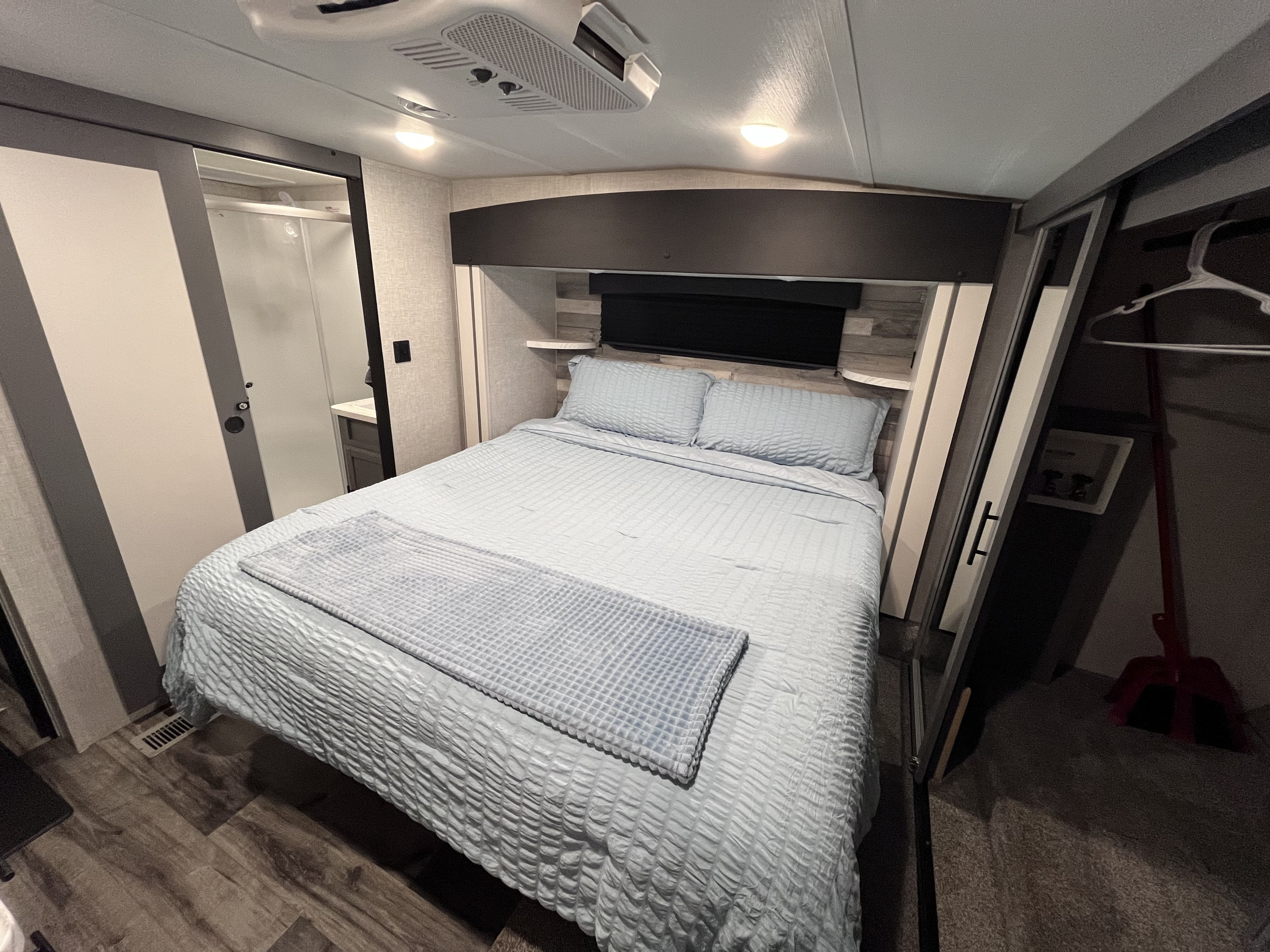 Modern RV rental bedroom interior features a light blue bed, built-in shelving, and space-saving sliding doors for comfort.. Volante 375MD 2023