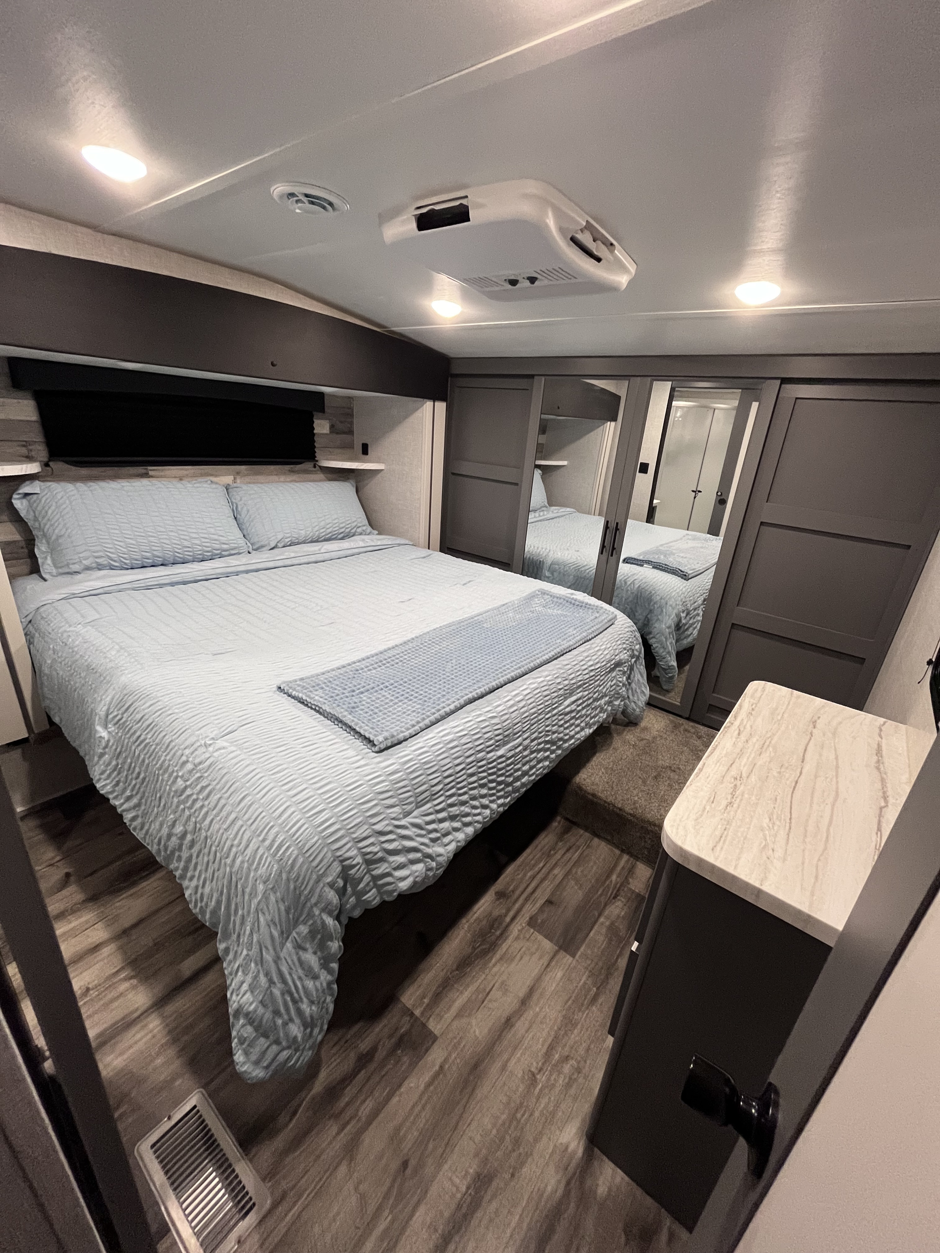 Explore this modern **RV rental** bedroom: a cozy blue bed, built-in storage with mirrored doors, and AC for comfort.. Volante 375MD 2023