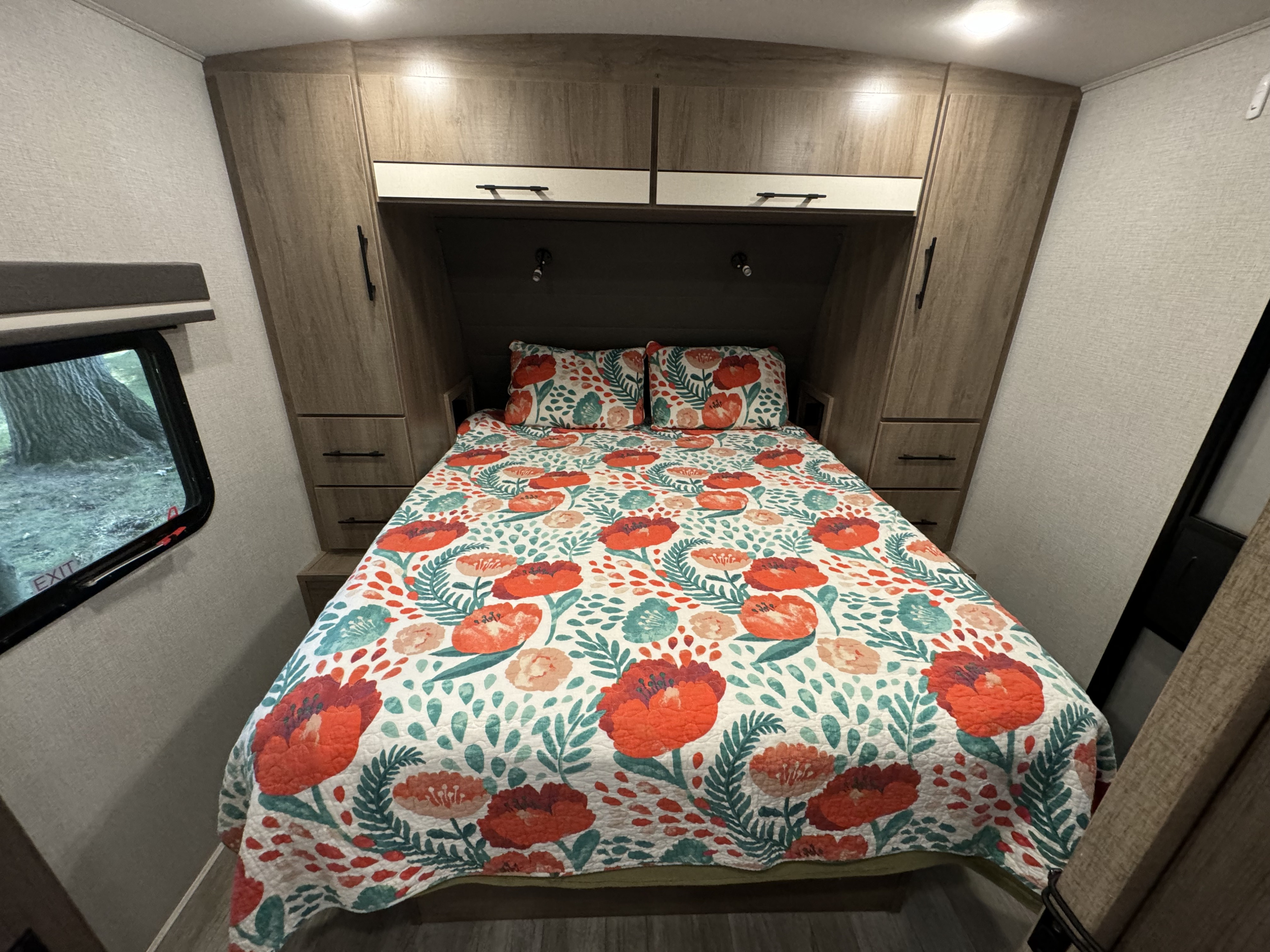 Inside an RV rental: a bright bedroom features a comfy bed with a cheerful floral comforter and built-in storage.. Grand Design Imagine 2024