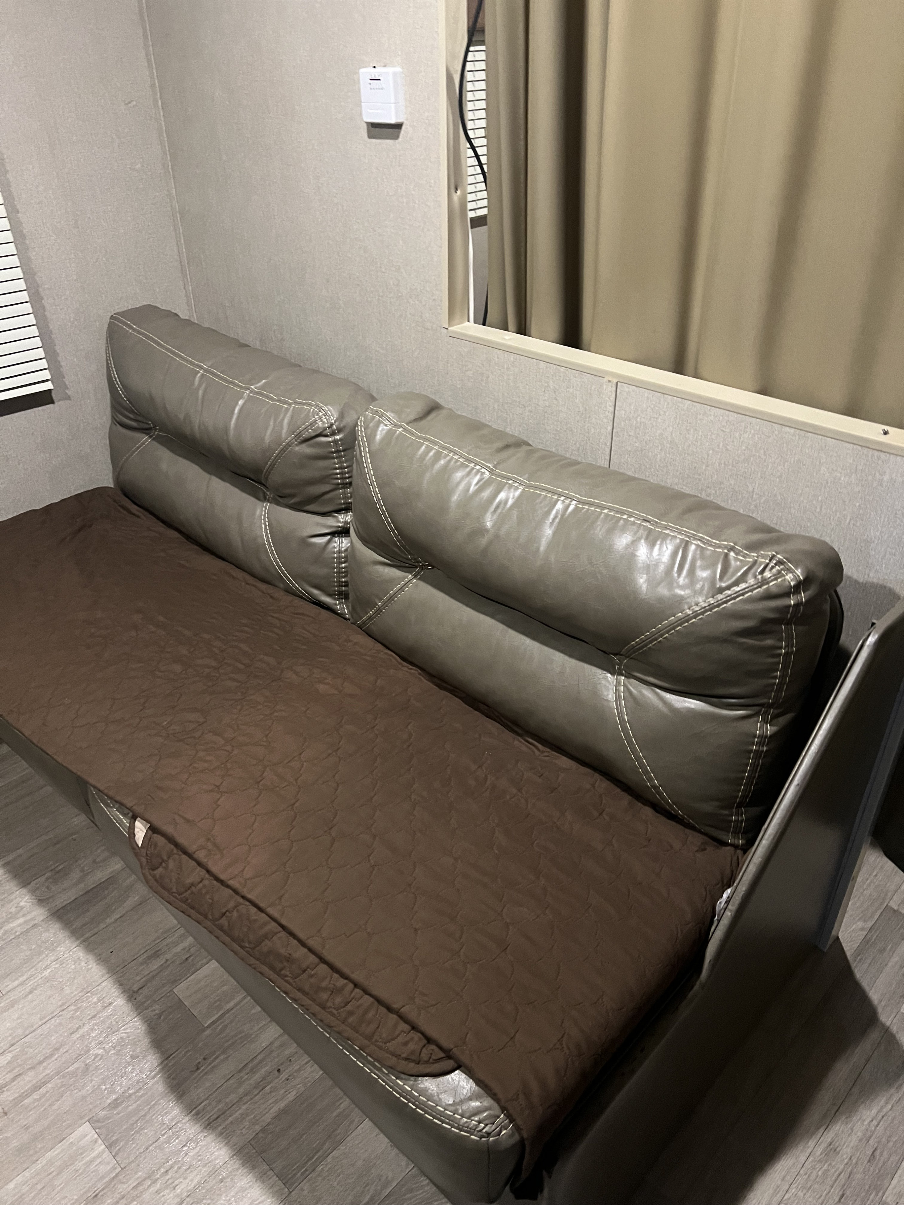 Grey faux leather RV rental sofa with a brown quilted cover, offering a comfortable seating area inside the vehicle.. Dutchmen Coleman Lantern LT 2016