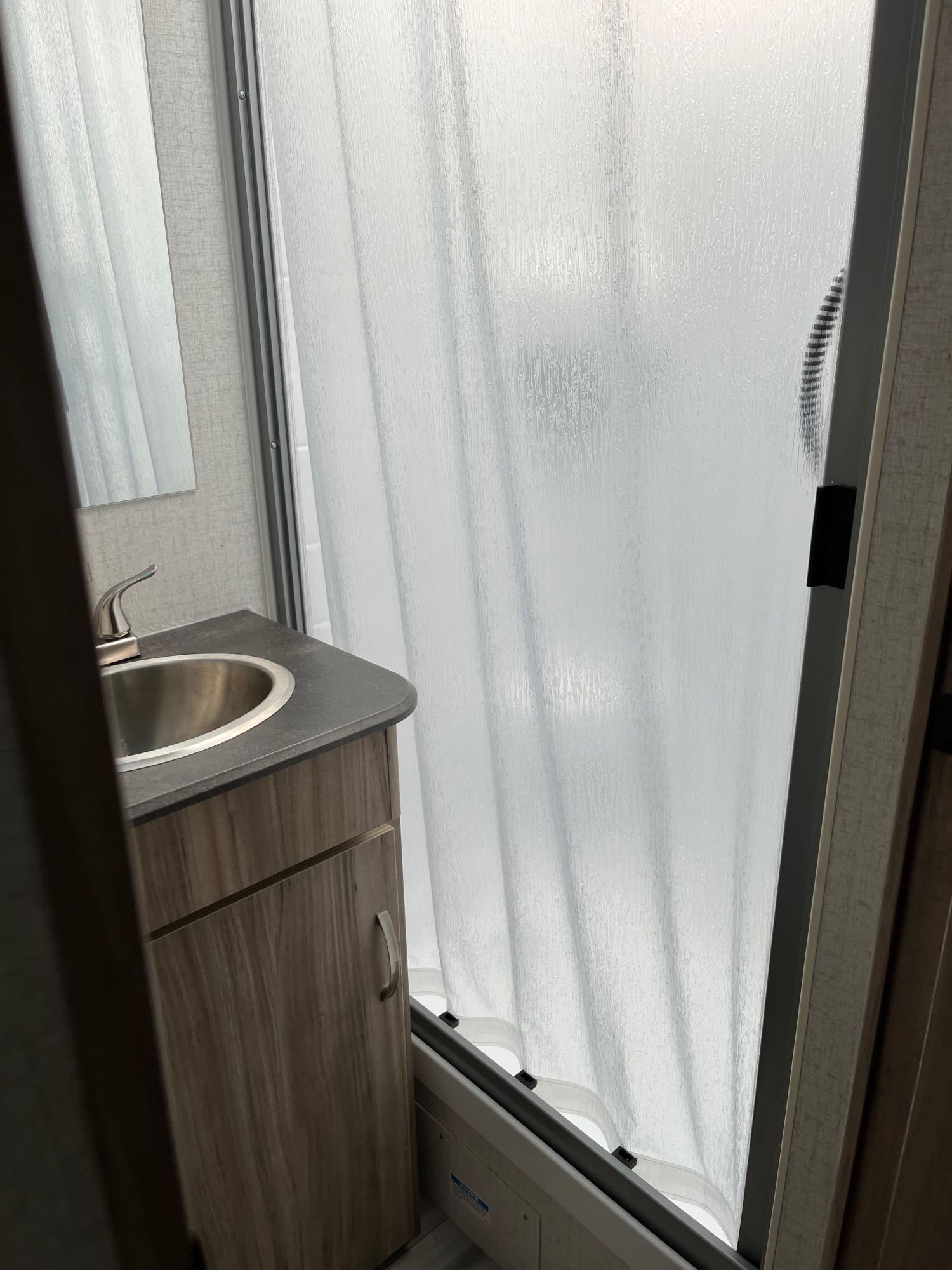 This rv rental bathroom features a vanity, sink, and faucet next to a textured, curved sliding shower door. A compact camper space.. Winnebago Minnie Winnie 2022