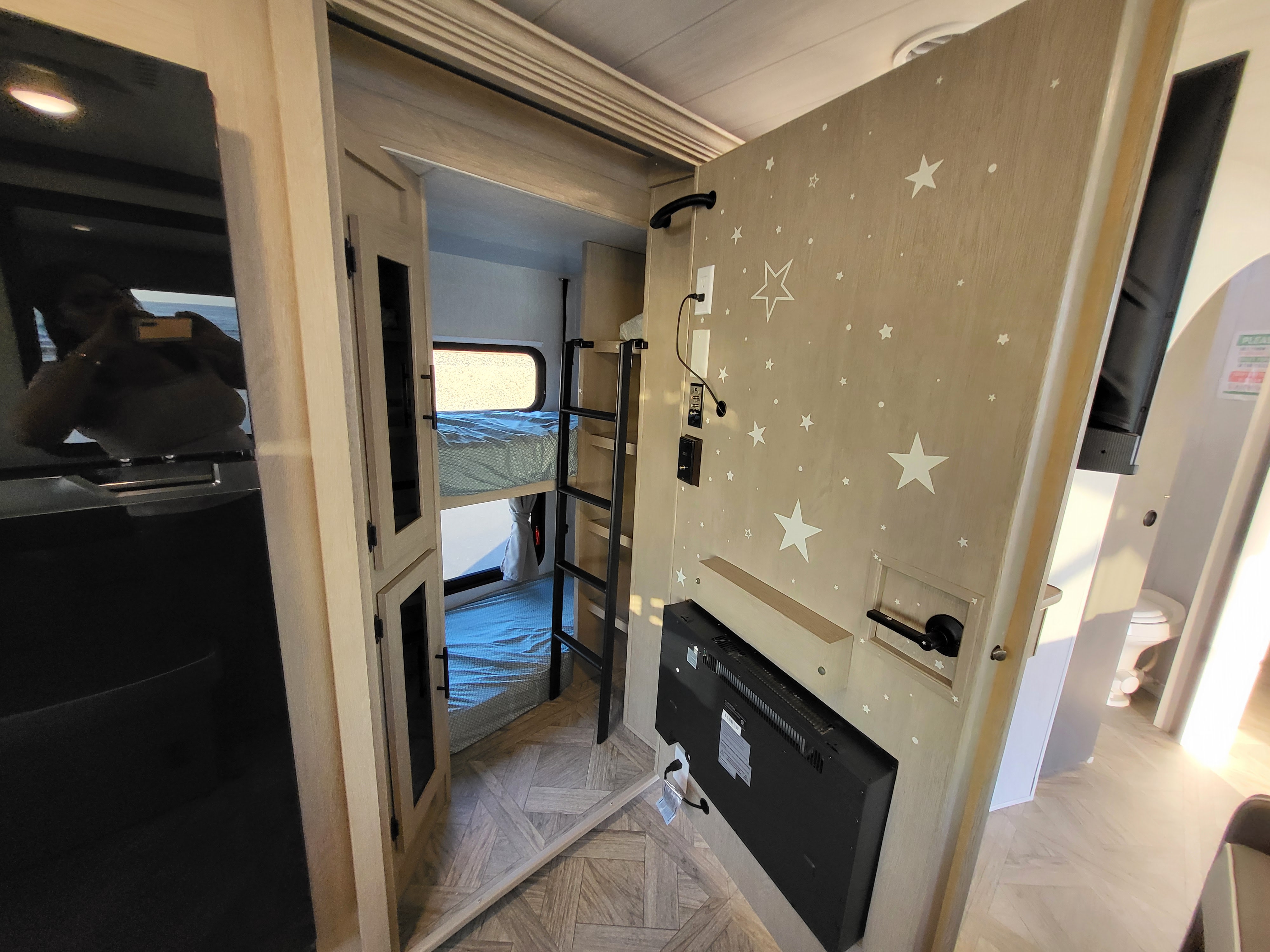 Cozy RV rental interior with bunk beds, ladder, a star-themed wall, mounted TV, and reflective cabinet surface.. Forest River Wildwood 24 view 2024