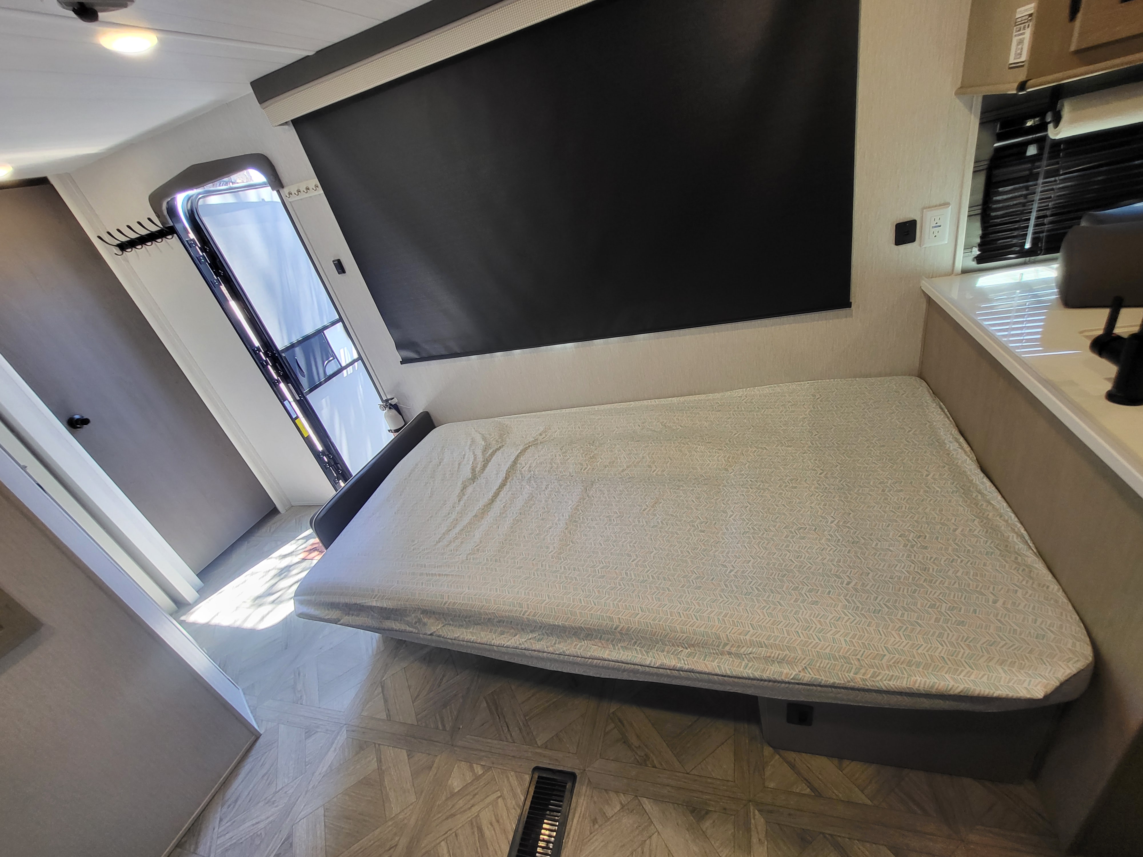 RV rental interior features a comfortable bed with patterned cover, a large window with black blind, and essential outlets.. Forest River Wildwood 24 view 2024