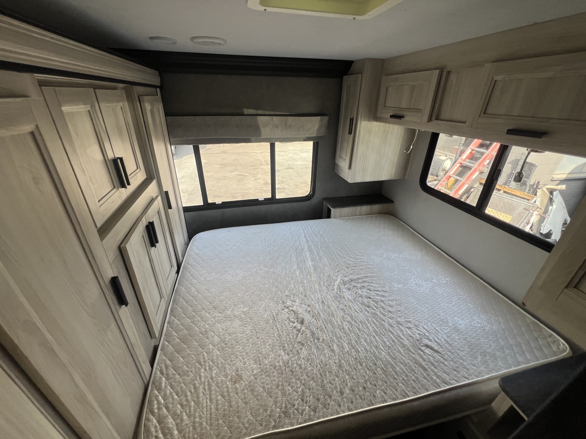 Cozy RV rental bedroom featuring a full mattress, overhead cabinets, and built-in storage on the left side.. Forest River Sunseeker LE 2021