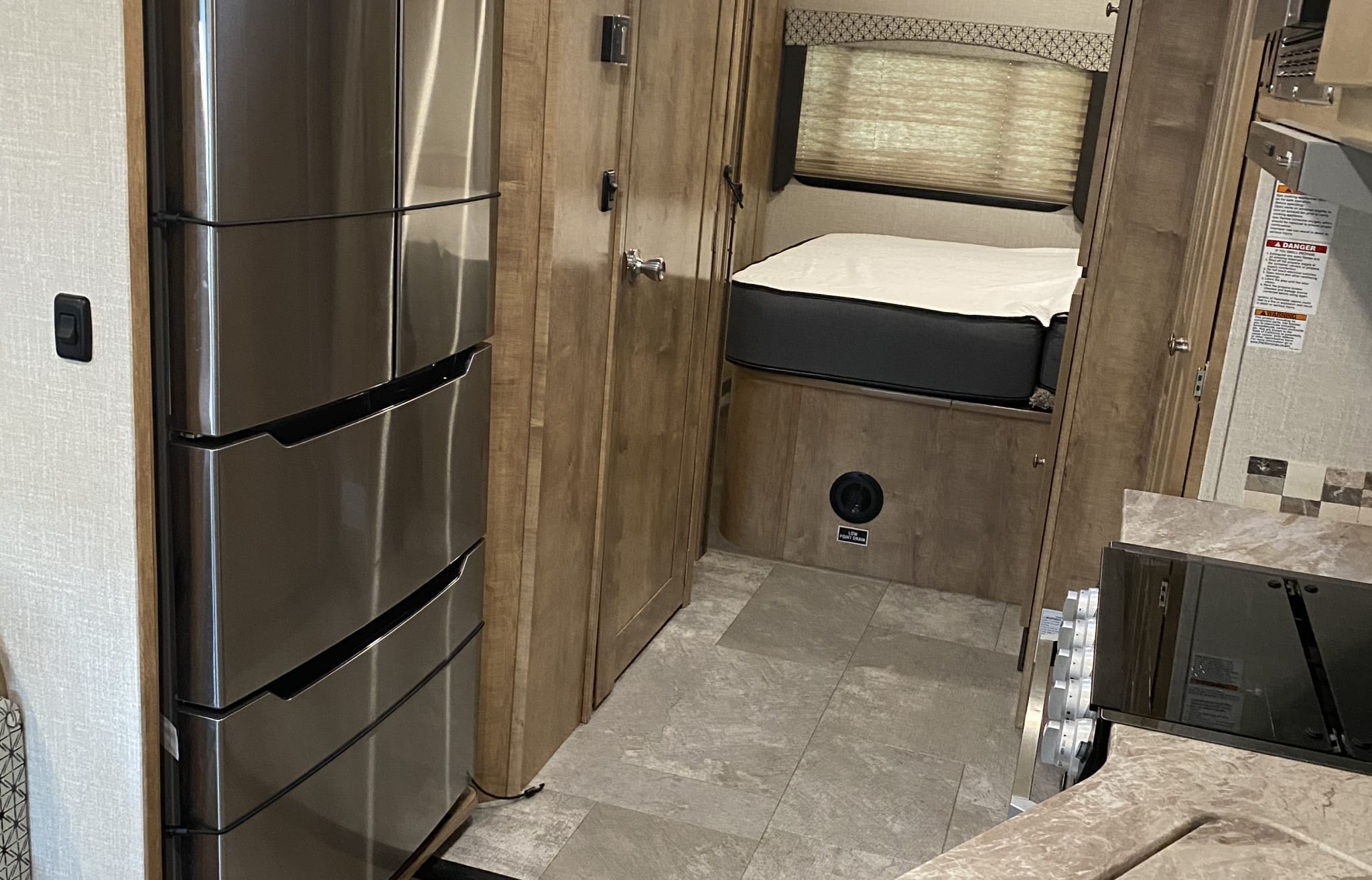Inside an RV rental: a compact interior showing a stainless steel fridge, a cozy bed, and a kitchenette counter with a stove.. Forest River Coachmen Leprechaun 2020