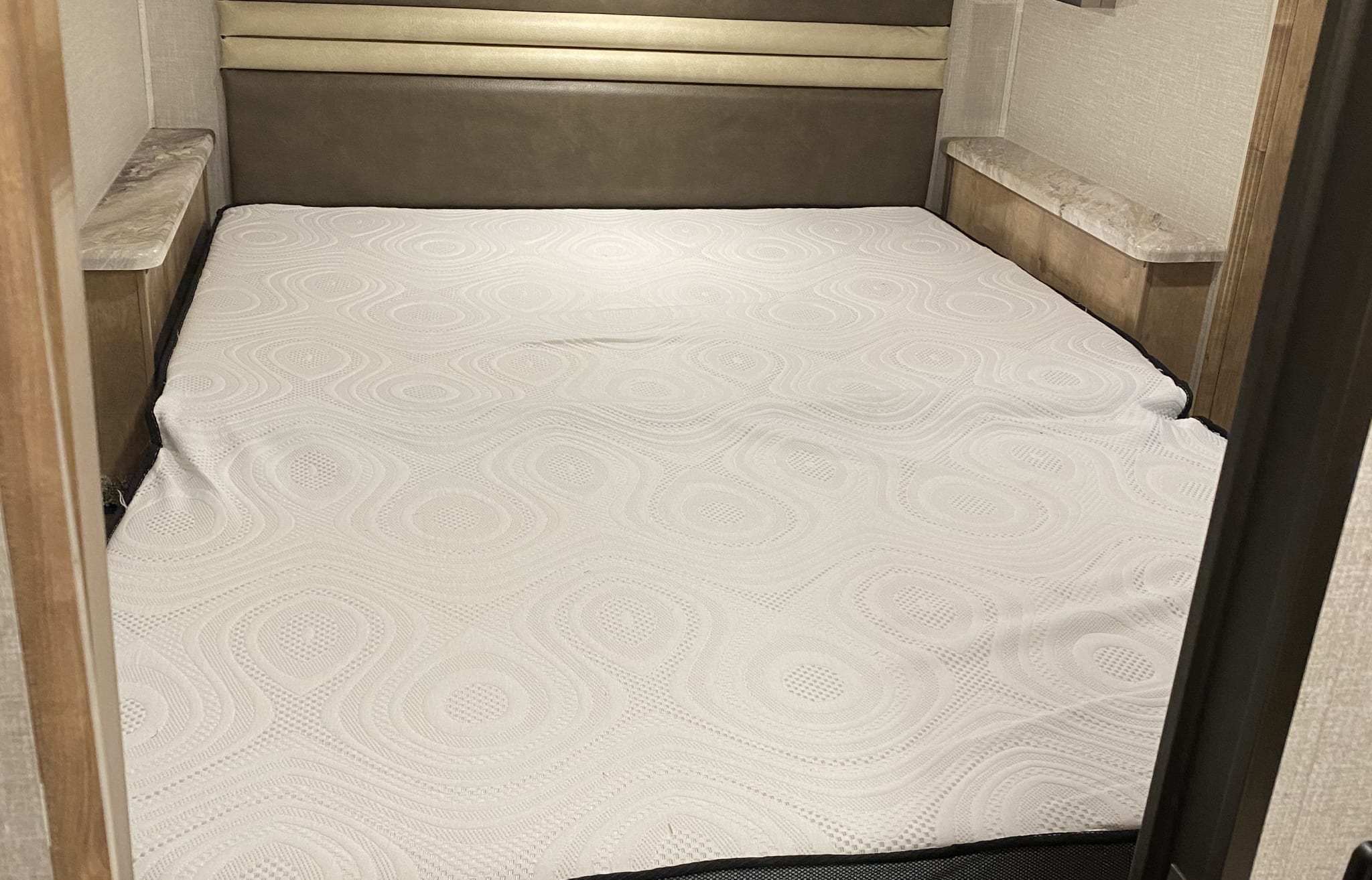 A comfortable bed in an RV rental, featuring a textured white mattress, upholstered headboard, and built-in side tables.. Forest River Coachmen Leprechaun 2020