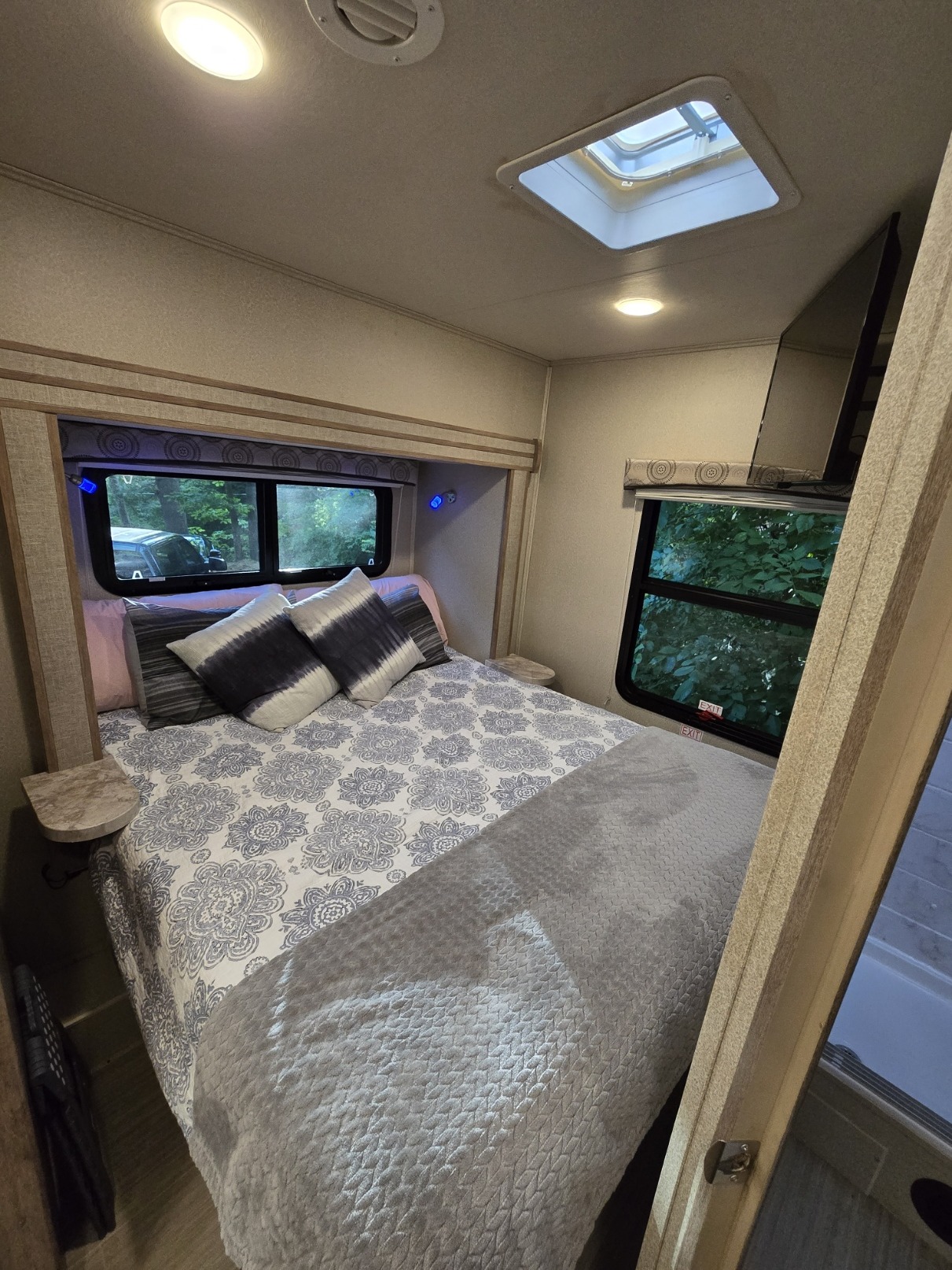 Bright RV rental bedroom: cozy bed with patterned duvet, skylight, windows showcasing lush trees, and small side tables.. Entegra Coach Odyssey 2020