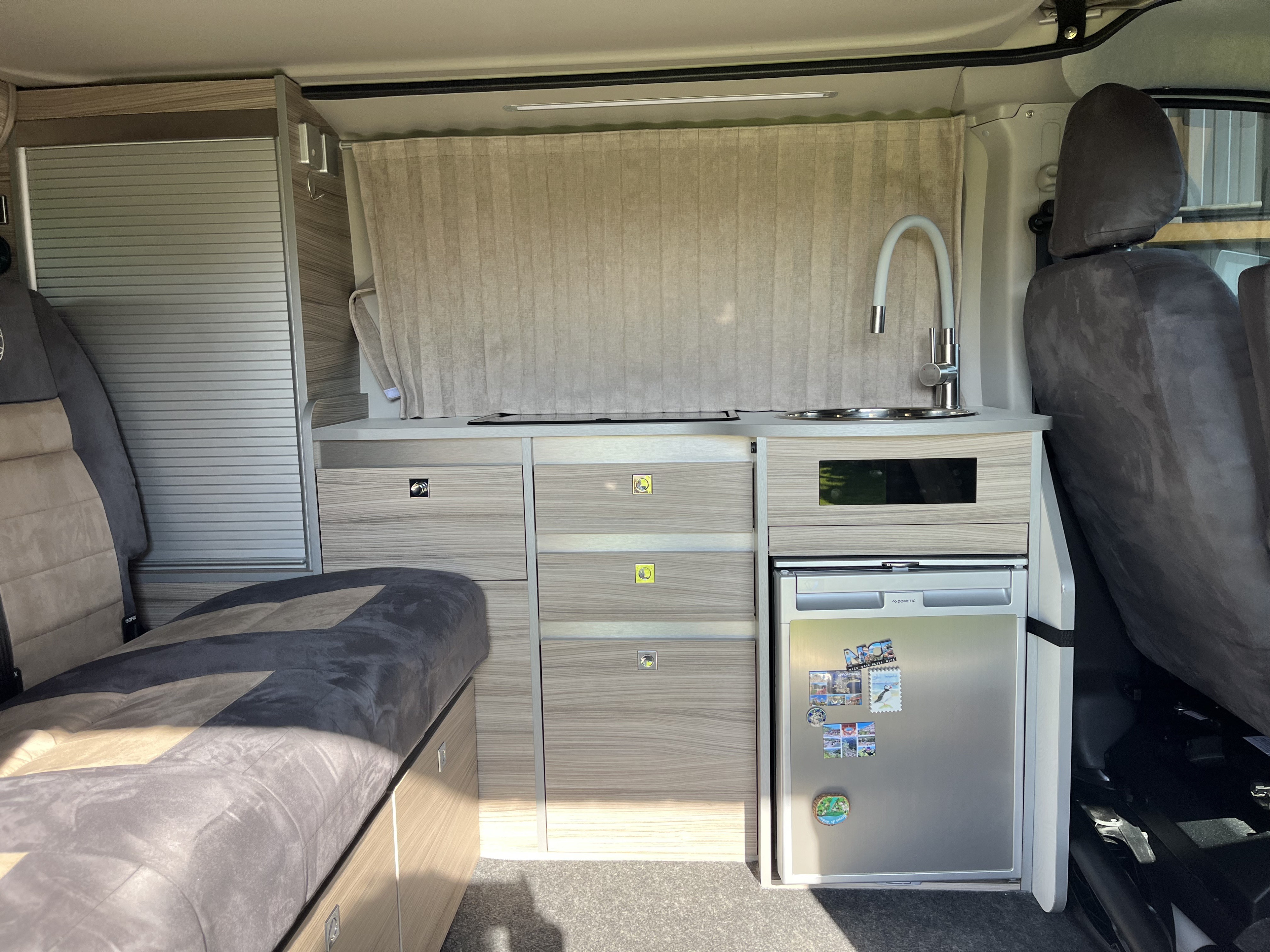 This rv rental features a cozy campervan interior with a compact kitchenette, sink, fridge, and sleeping area, perfect for travel.. Renault Trafic Glénan, HorizonVan 5 2024