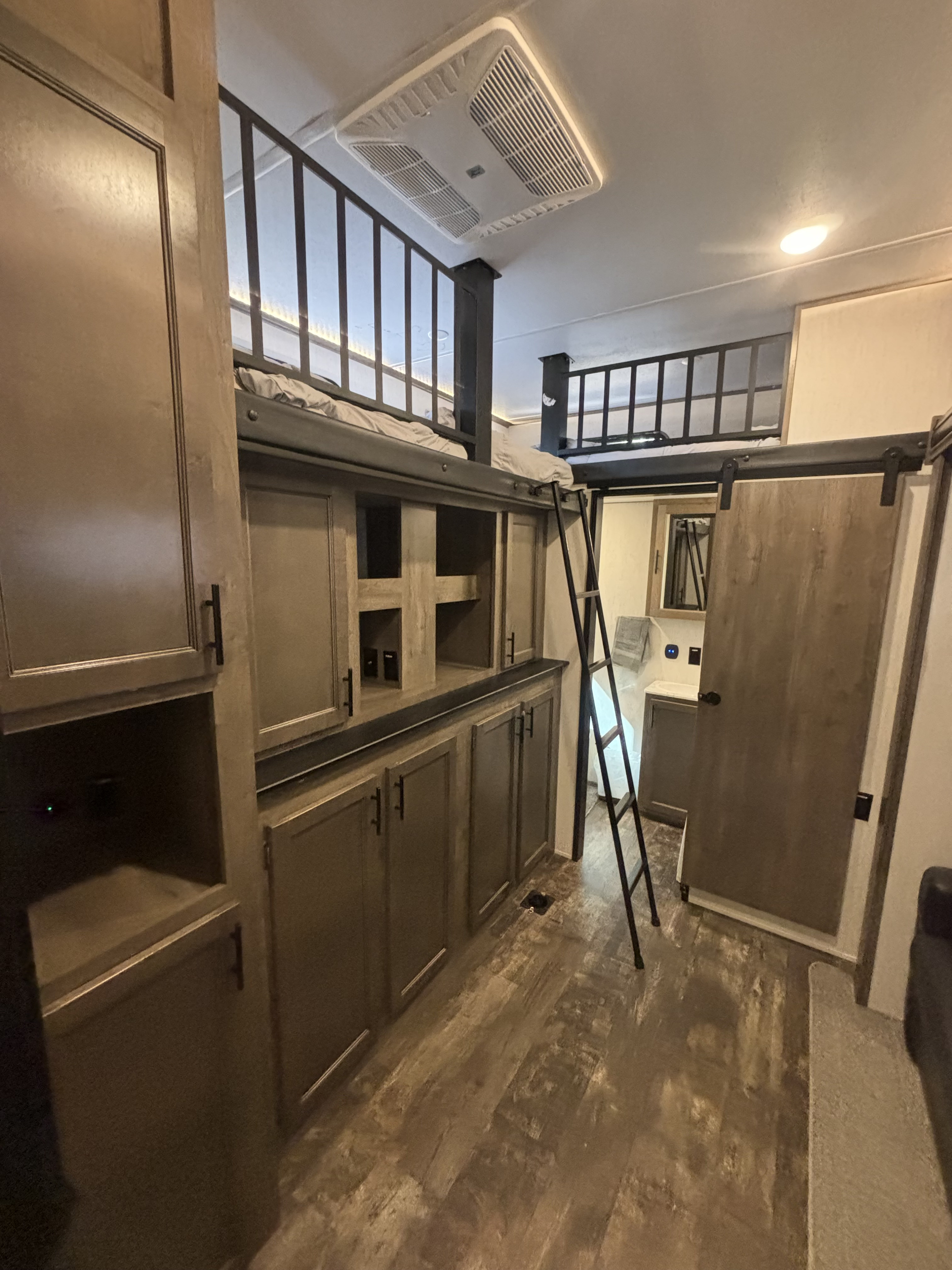 RV rental interior: A wooden loft bed with a ladder overlooks built-in storage. A barn door slides to reveal the bathroom.. Forest River Sabre 2022