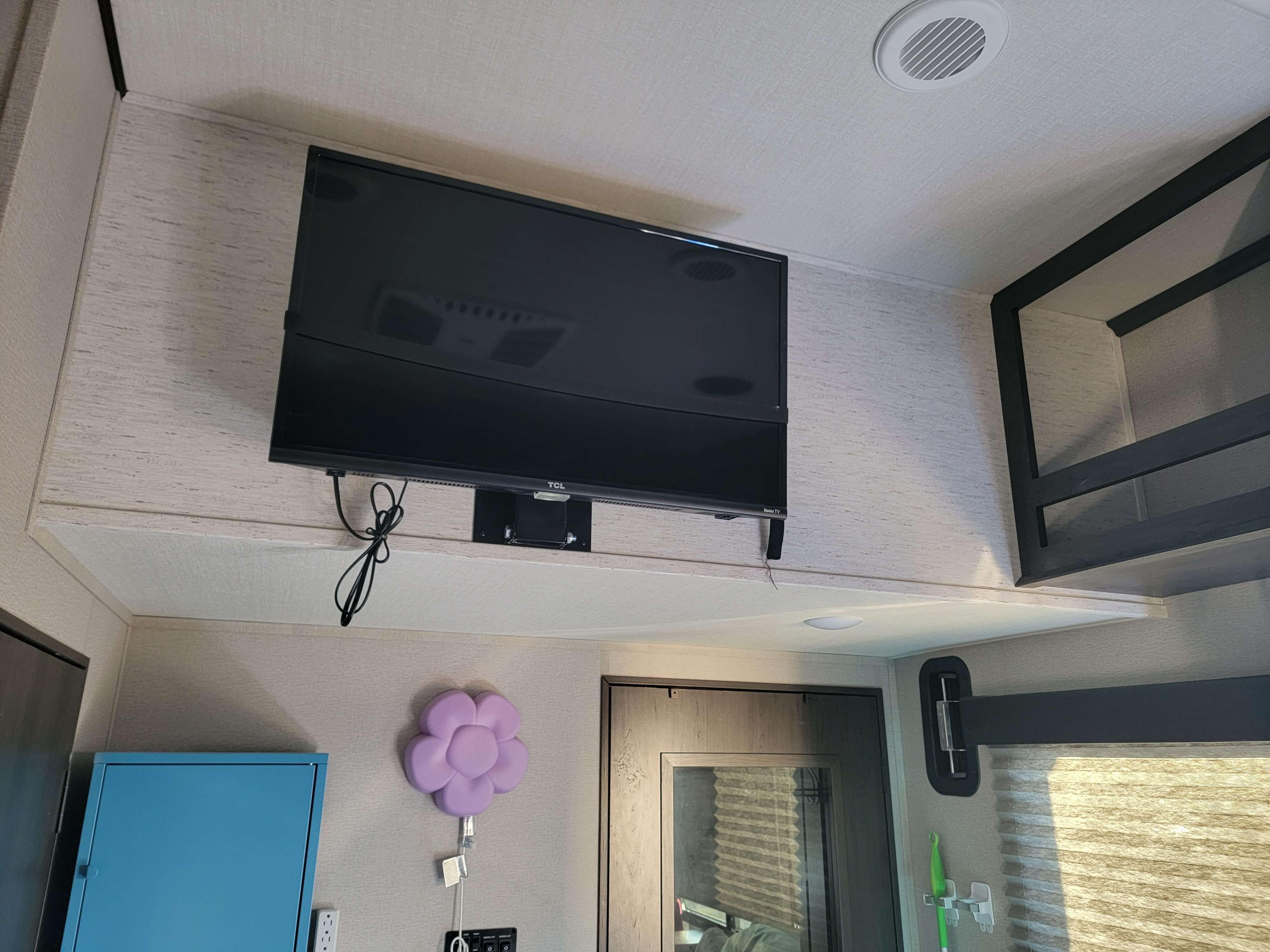 Inside an RV rental: a mounted TV above a shelf, ceiling vent, bunk bed on right, and storage cabinets.. Grand Design Momentum 2022