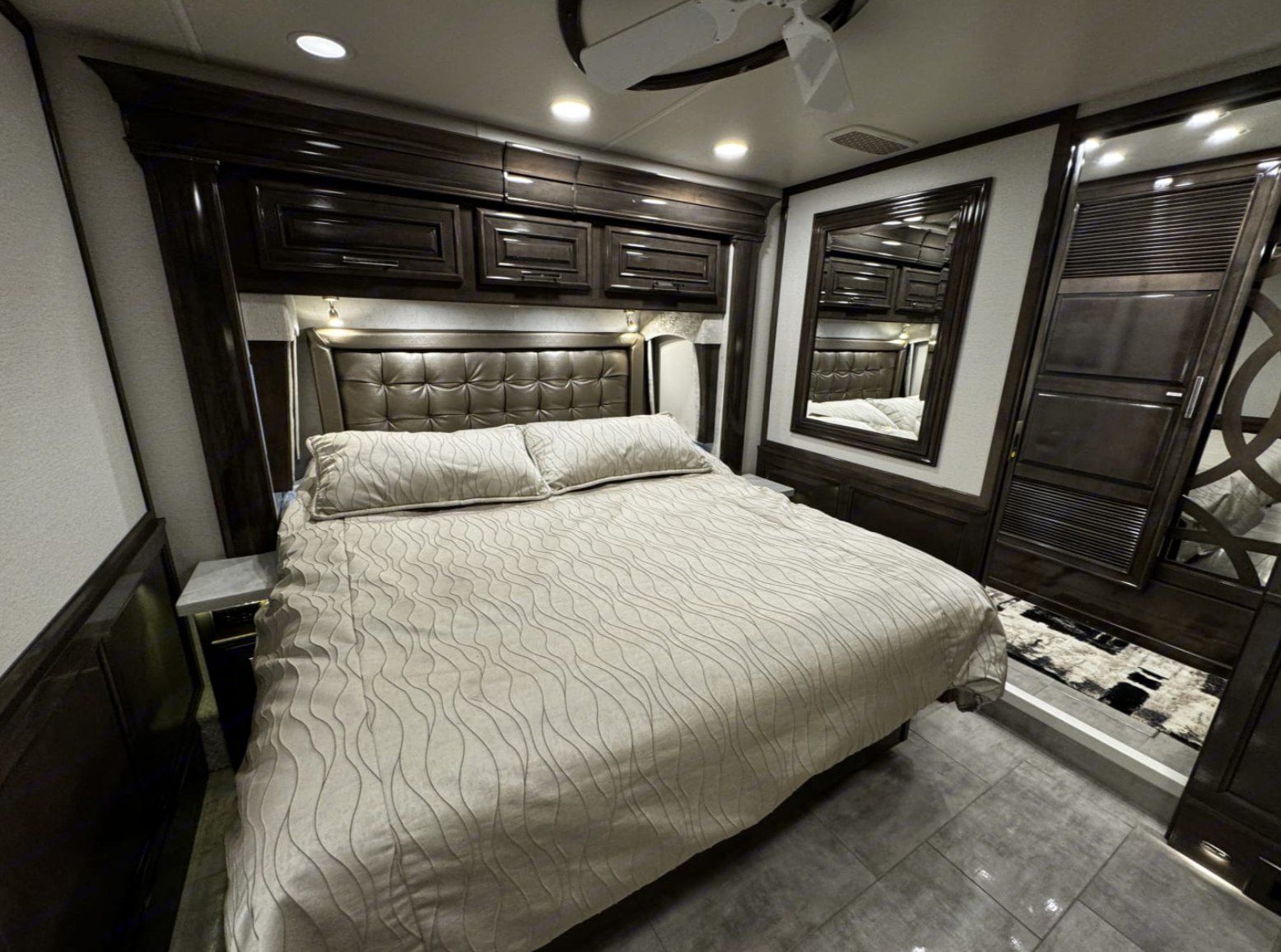 Experience comfort in this luxurious RV rental bedroom, featuring dark wood, a plush bed, and overhead storage. Ideal for travel.. Entegra Coach Anthem 44R 2022