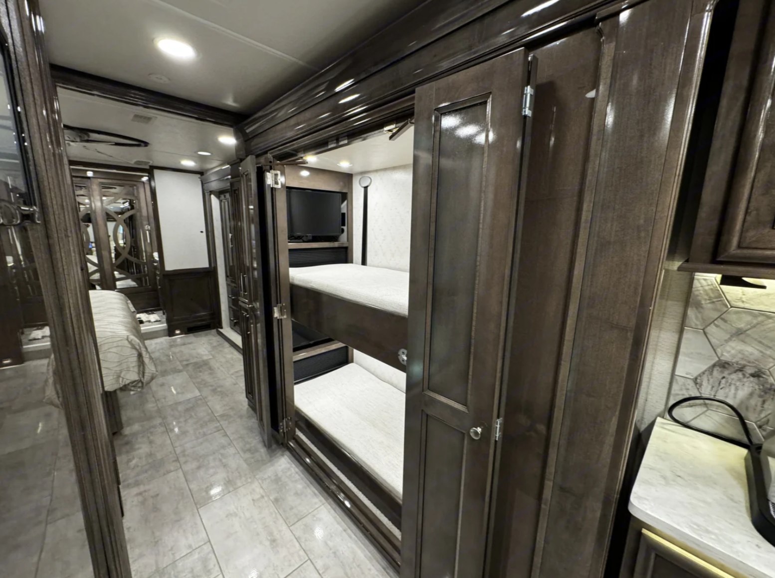 Spacious RV rental interior featuring modern bunk beds, a TV, and sleek dark wood cabinetry. Tiled floor throughout.. Entegra Coach Anthem 44R 2022