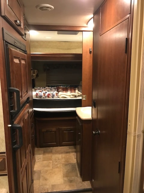 RV rental interior with a compact fridge, tiled floor hallway, and a cozy bedroom area visible beyond.. Forest River Solera 24R 2014