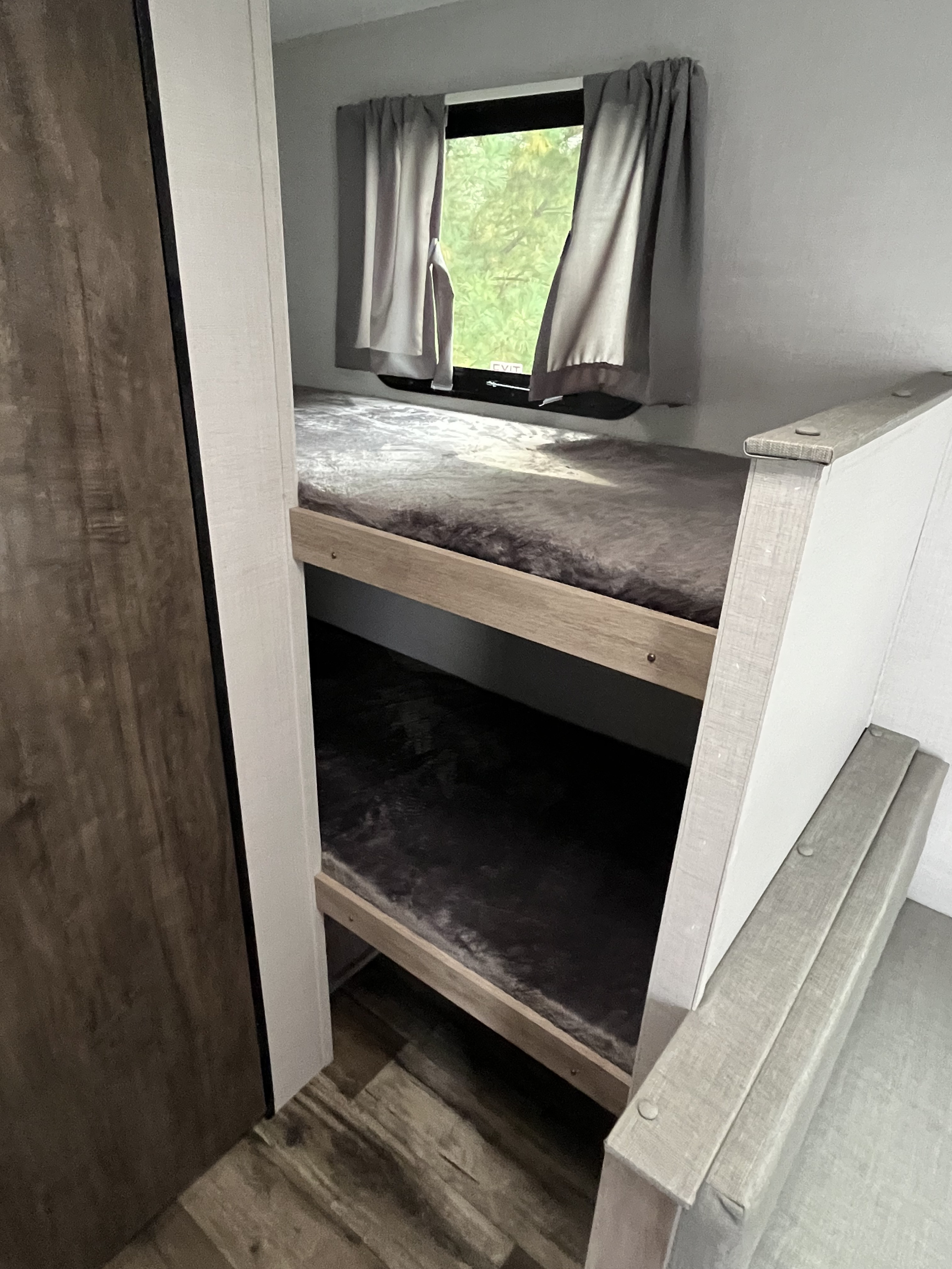 RV rental: Cozy bunk beds in a compact interior. A window above features gray curtains, an exit sign, and a view of trees.. Gulf Stream grand river 2024