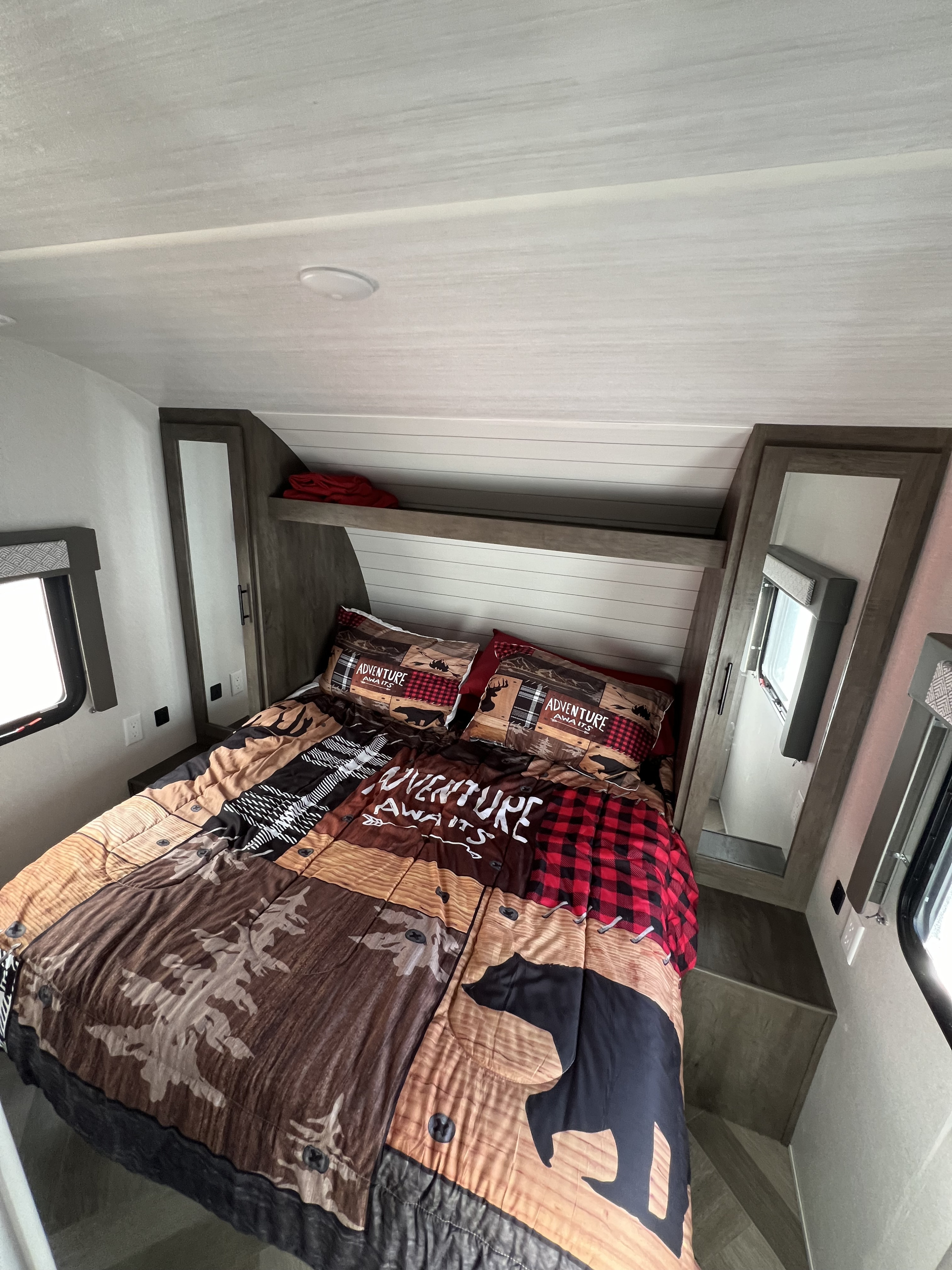RV rental interior: A cozy bedroom featuring "Adventure Awaits" rustic bedding, windows, and compact storage.. Forest River Wildwood X-Lite 2020