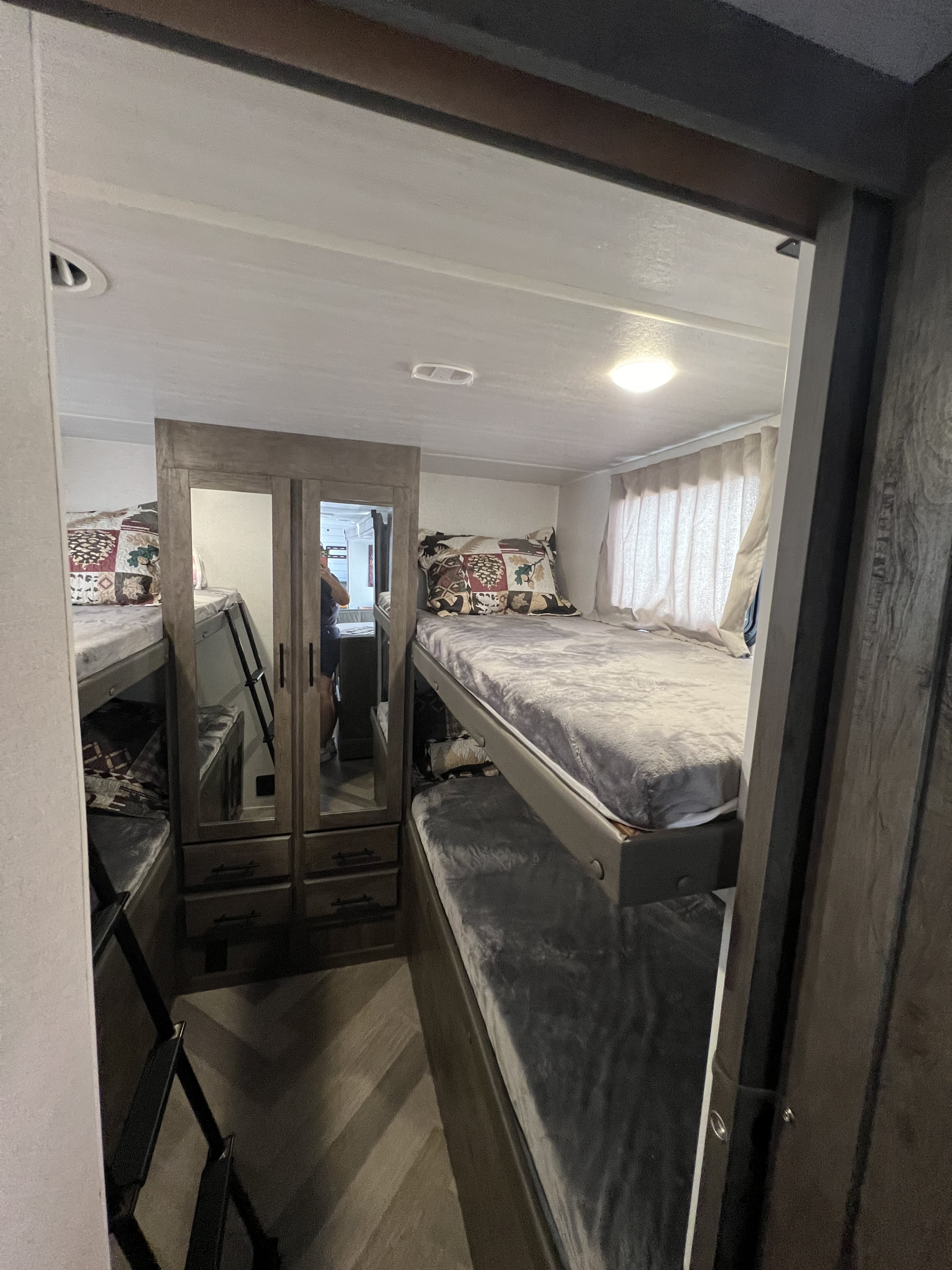 RV rental bunkhouse: A compact bedroom with multiple cozy bunk beds, a central mirrored wardrobe, and curtained windows.. Forest River Wildwood X-Lite 2020