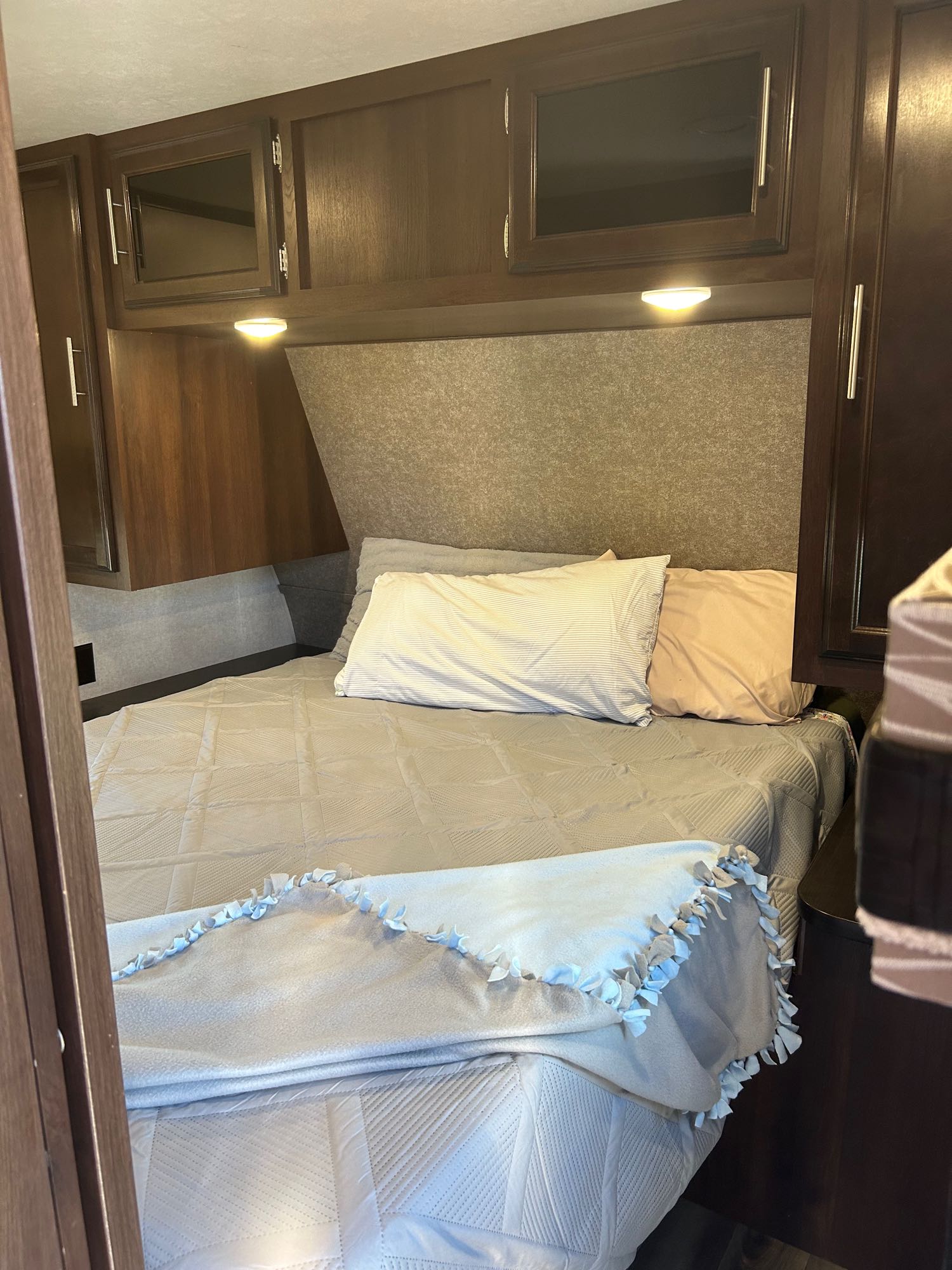 Cozy RV rental bedroom with a neatly made bed, pillows, blankets, and wooden overhead storage.. Jayco Jay Flight 2019