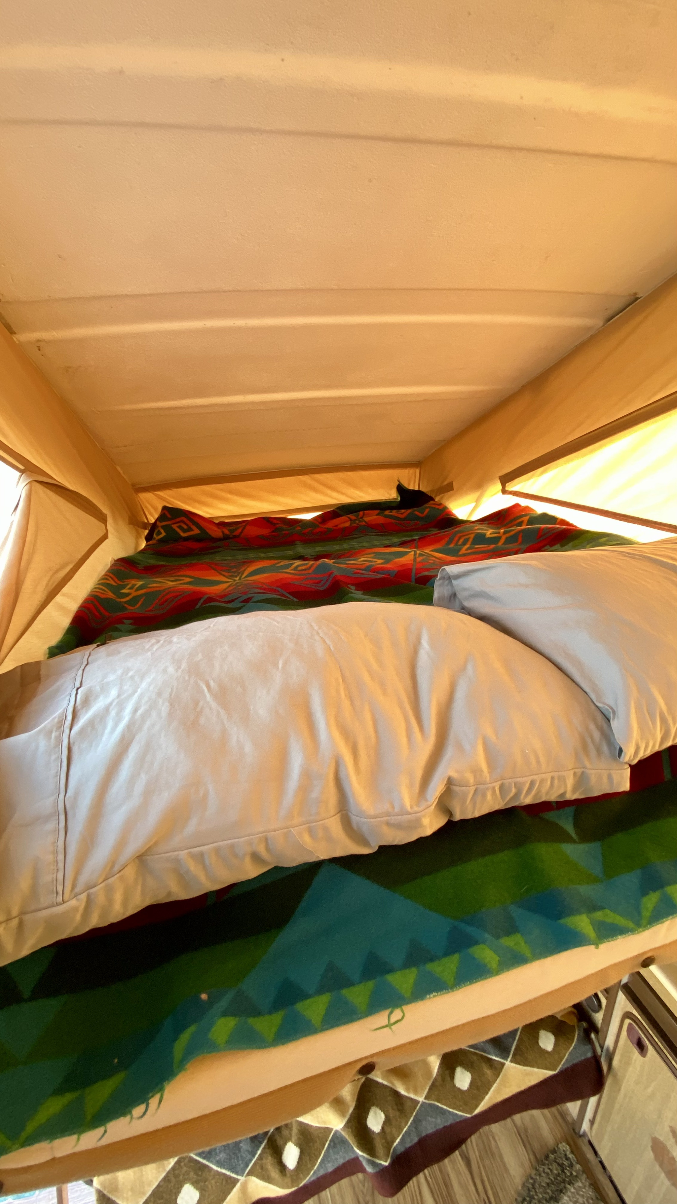 Cozy pop-top bed inside an RV rental, featuring colorful blankets and pillows, ideal for travel adventures.. Volkswagen T3 Westfalia 1981