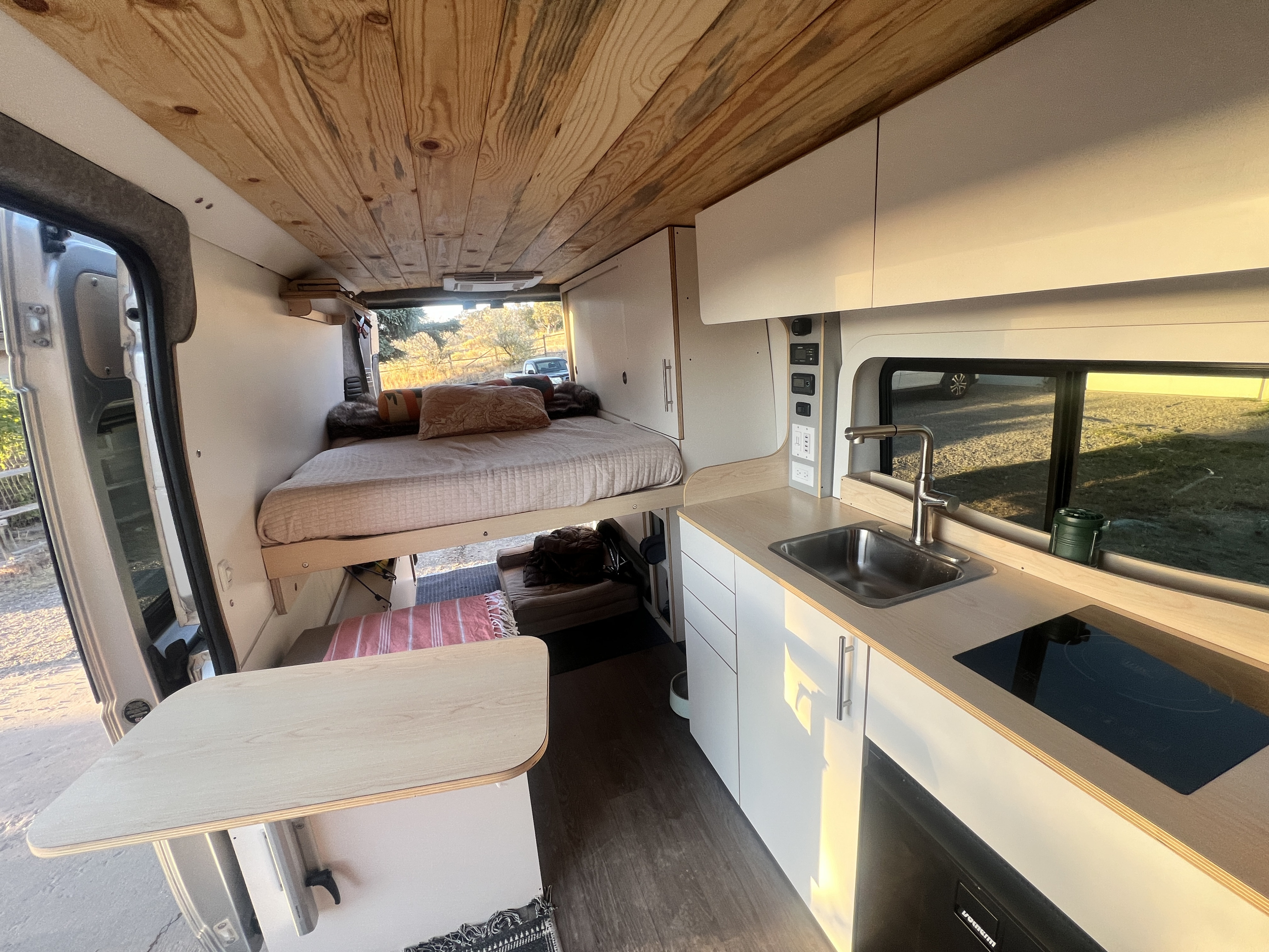 Inside a custom RV rental camper van, featuring an elevated bed, full kitchenette, and dining table.. Dave & Matt Vans Dave & Matt Vans Class B 2024