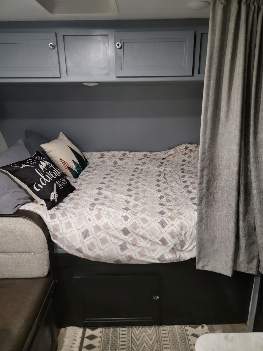 Cozy RV rental interior showing patterned bed, overhead storage, and privacy curtain for a comfortable stay.. Winnebago Minnie Winnie 2021