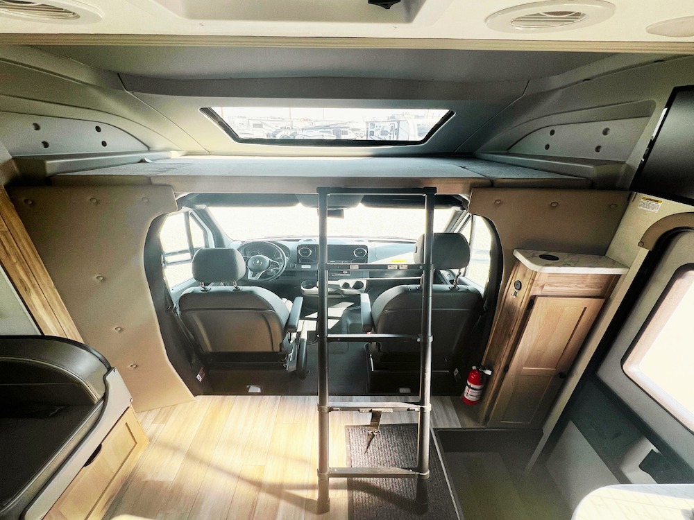 Inside an RV rental: a cozy interior featuring an overhead bunk with ladder, front cab, and functional living space.. Coachmen Prism 24FS 2024
