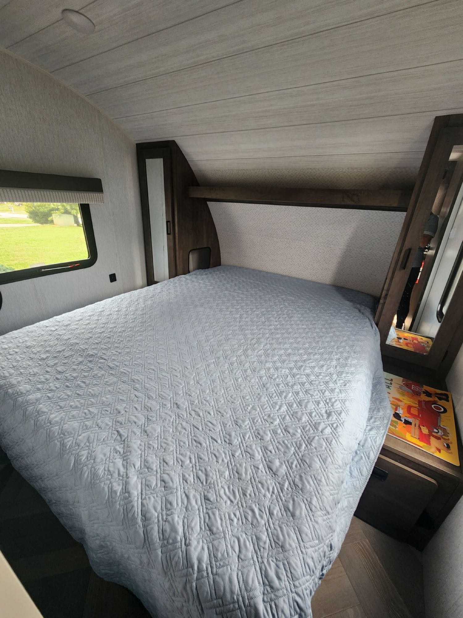 Cozy RV rental bedroom with a light blue quilted bed, window offering green views, and practical built-in storage for comfortable travel.. Forest River Salem Cruise Lite 2022