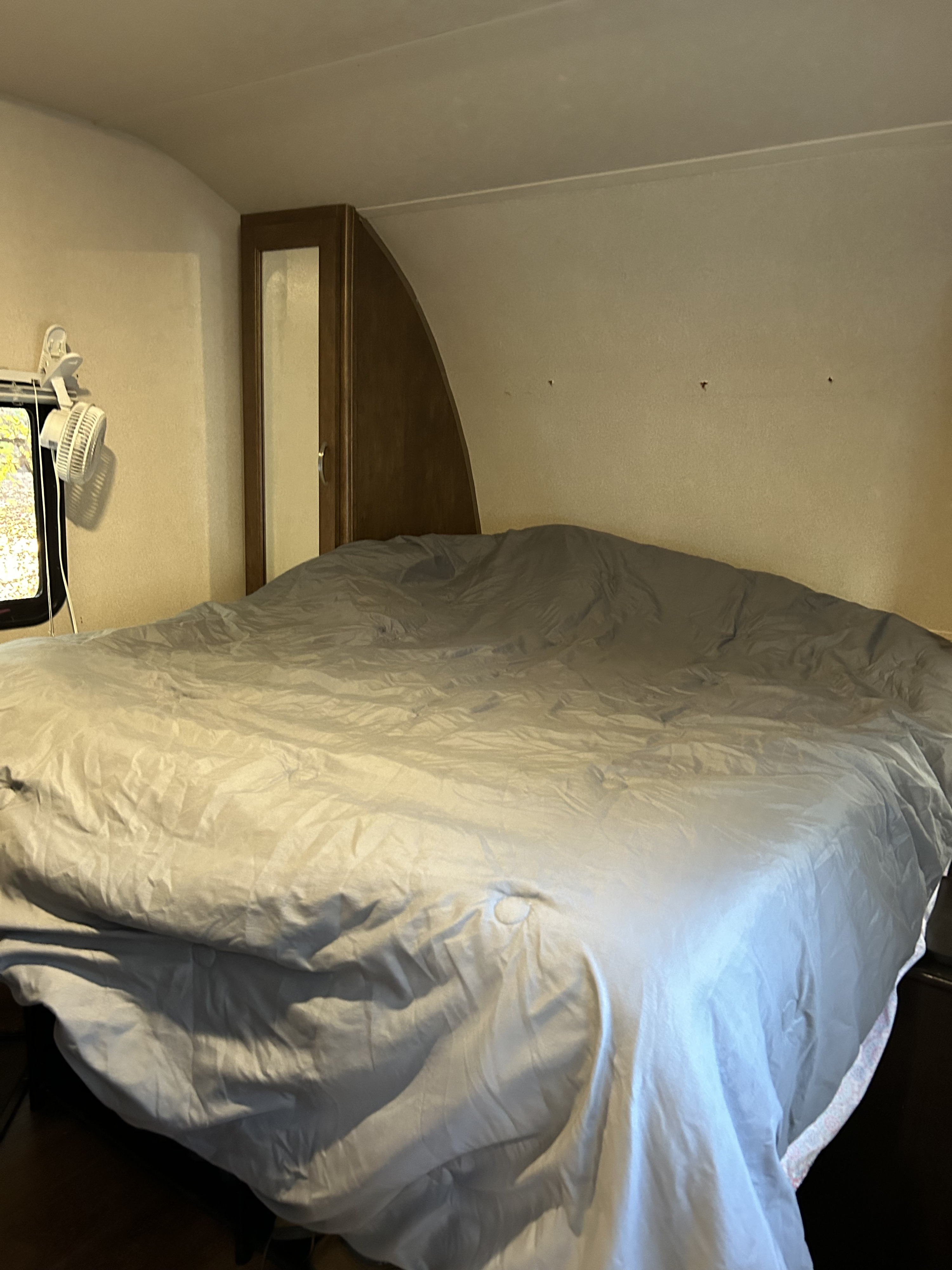RV rental bedroom showcasing a large grey bed, clip-on fan by a window, and wood storage unit with a mirror.. Forest River Wildwood 2018