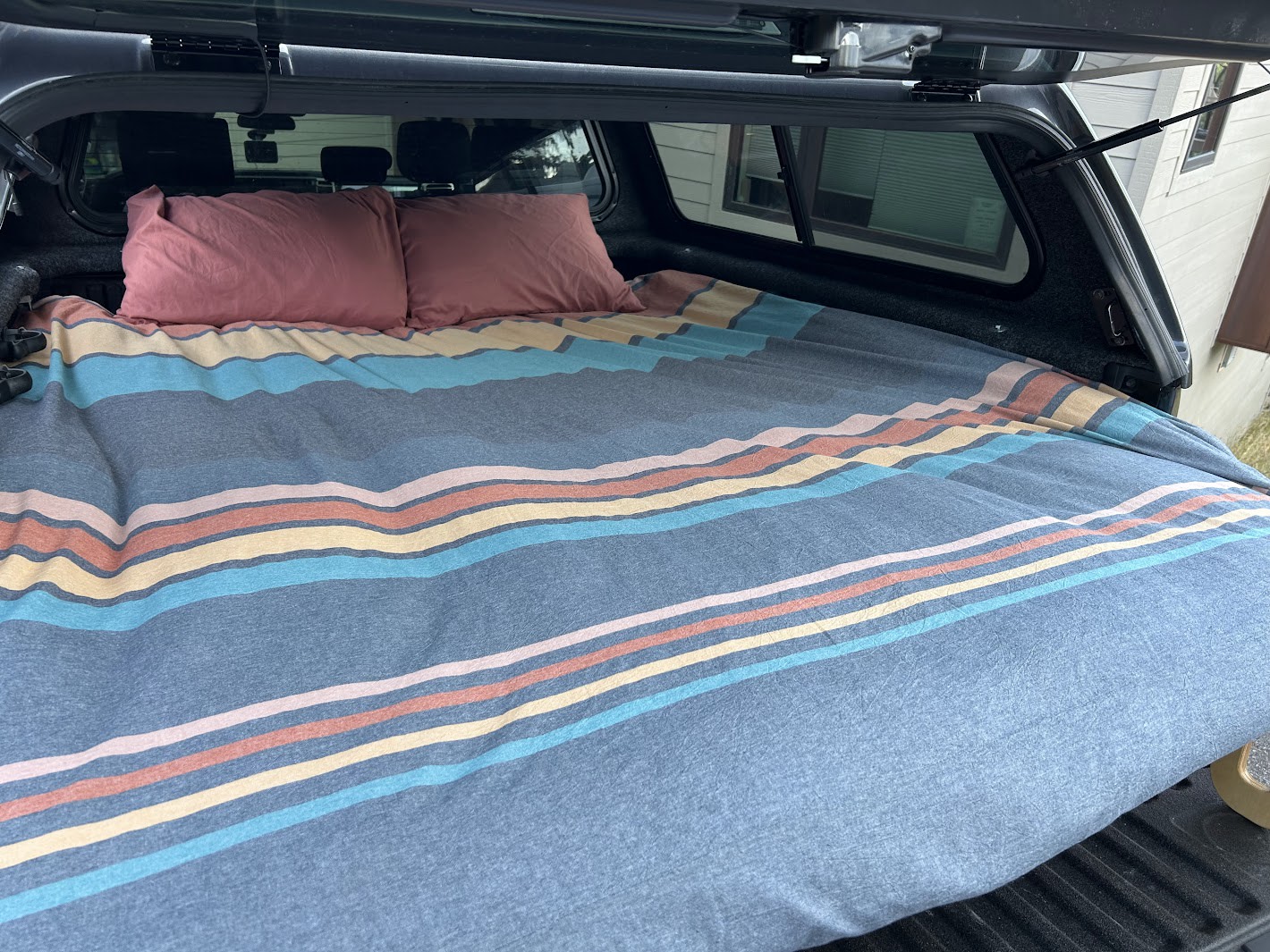 This cozy rv rental truck camper features a comfortable bed with a colorful striped blanket and pillows, ideal for camping.. Other Other 2024