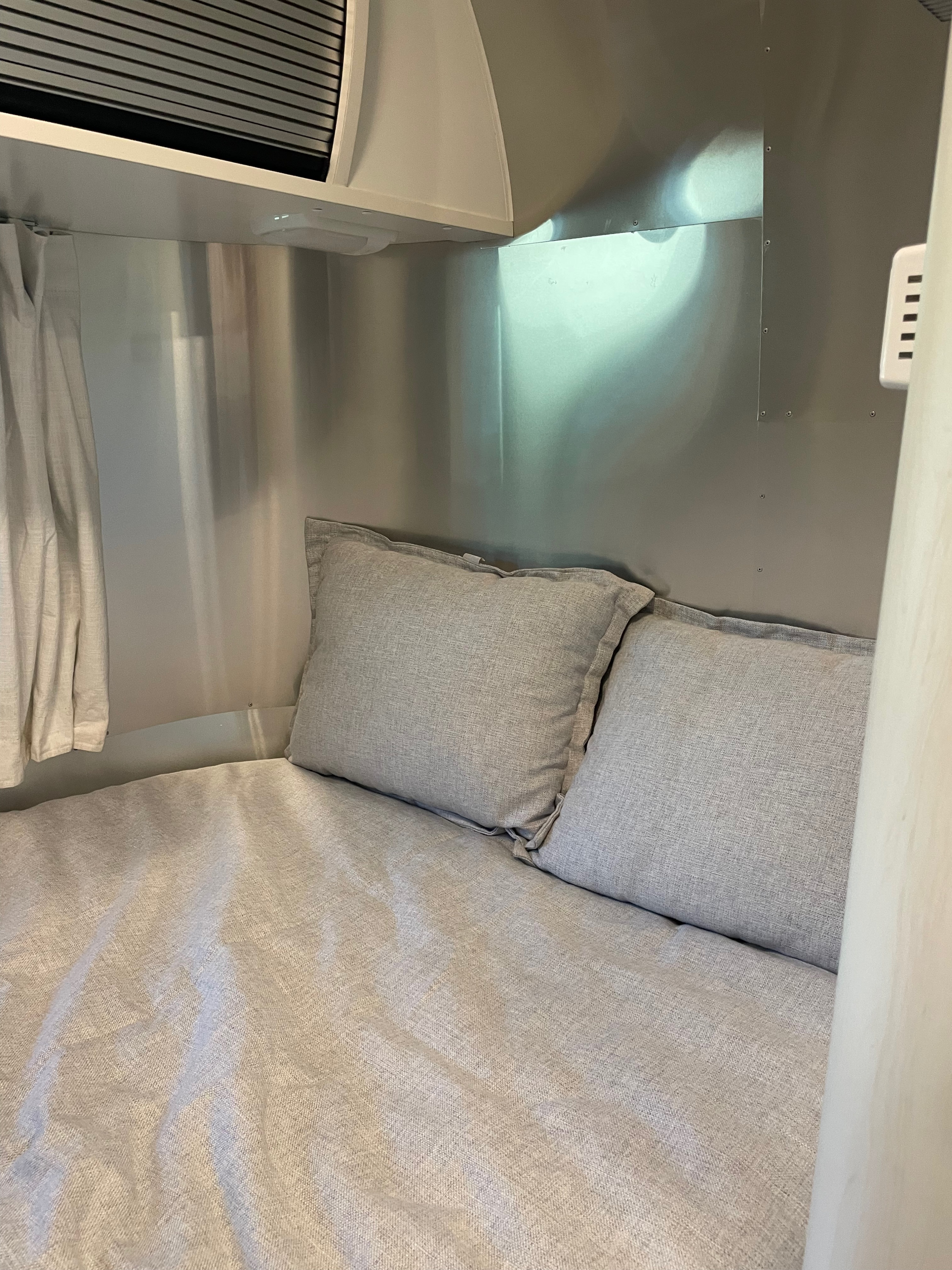 Cozy RV rental bed with light gray linen bedding and pillows, set within a sleek metallic travel trailer interior.. Airstream Bambi 2022