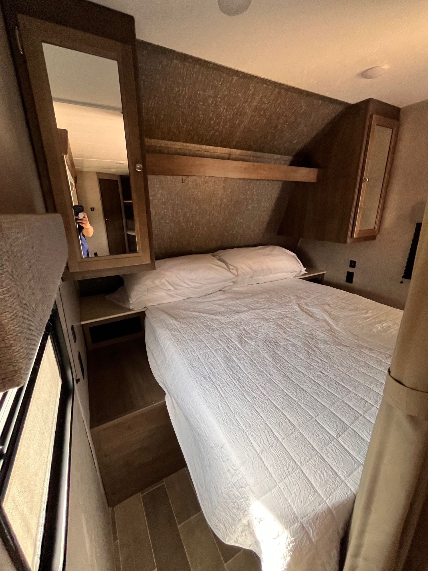 Compact RV rental bedroom with white bed, overhead shelf, and mirrored cabinet.. Dutchmen Coleman Lantern 2019