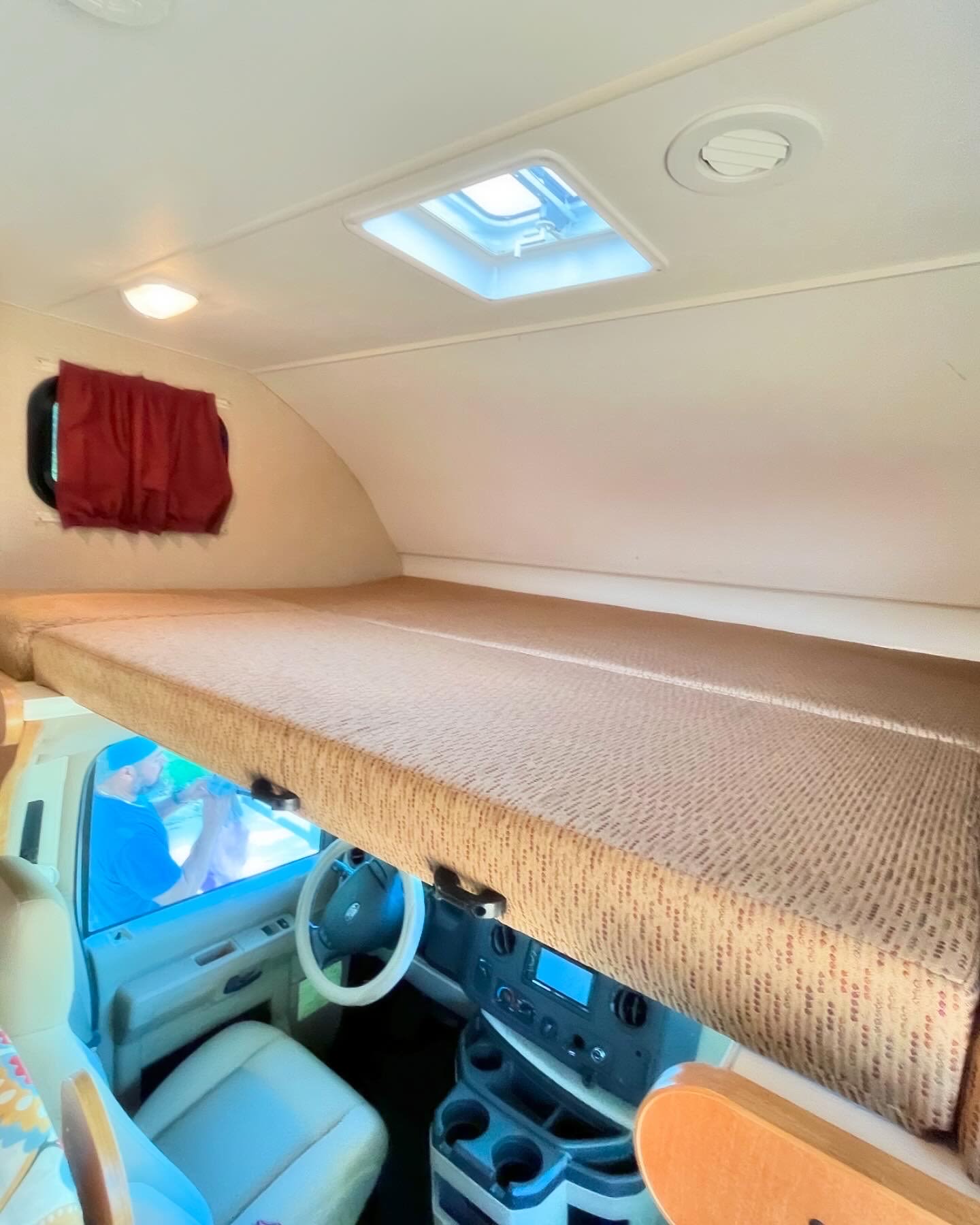 Inside an RV rental: a comfy over-cab bunk bed. Ideal for road trip adventures, with skylight and driver's cabin visible.. Itasca Spirit 2015