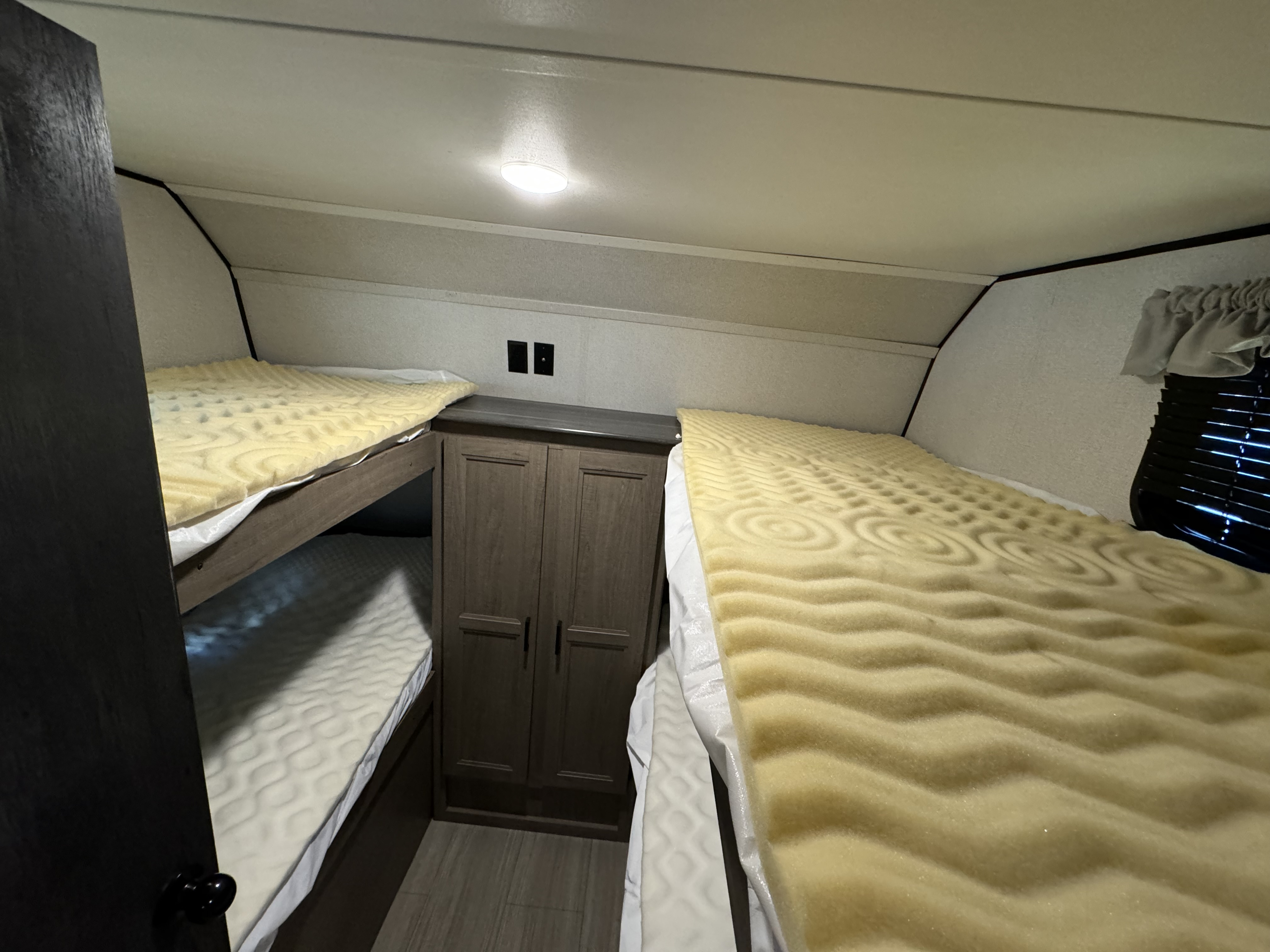 Cozy RV rental sleeping area featuring two bunk beds with yellow foam toppers and a central storage cabinet.. Keystone Hideout 2021