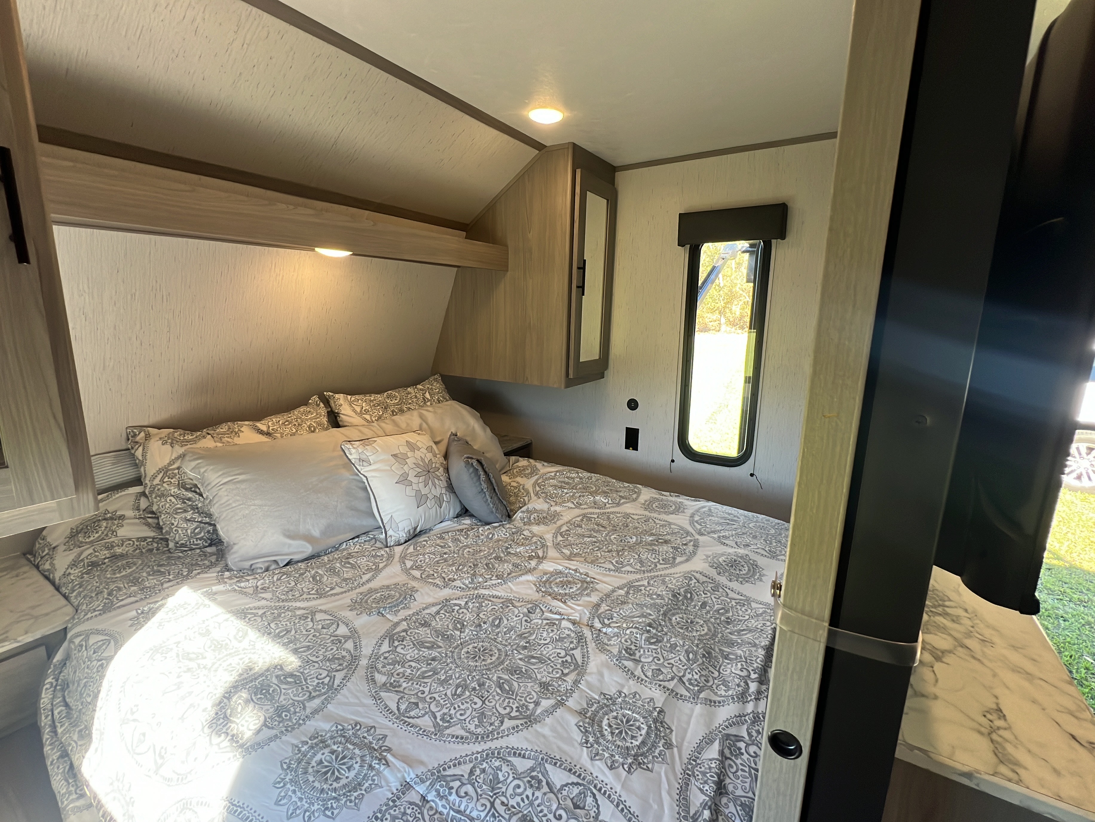 RV rental bedroom: a cozy space with a large bed, patterned bedding, overhead cabinets, and a window.. Dutchmen Coleman Lantern 2023
