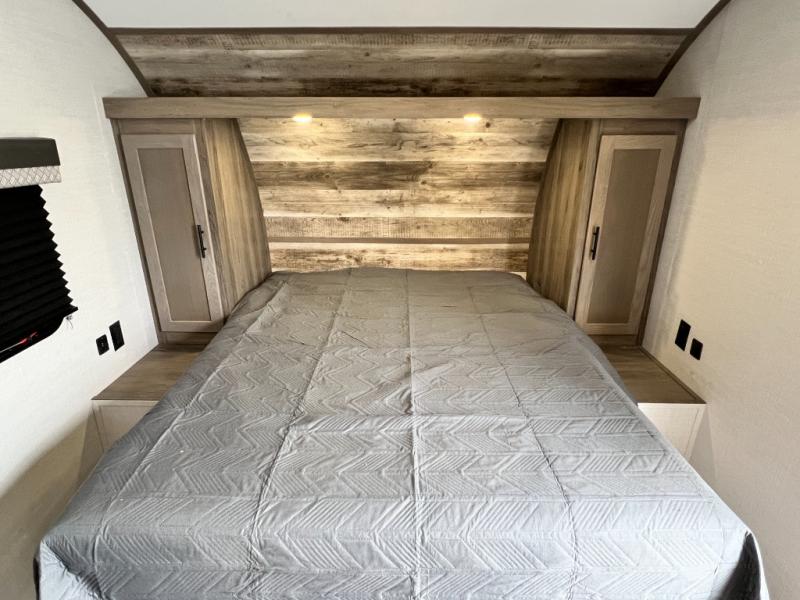 Comfortable RV bedroom with a grey bed, wood-paneled headboard, and side cabinets. Perfect for an RV rental getaway.. Gulf Stream Ameri-Lite 2022