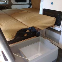 RV rental interior features a tan bed, microwave, and cooler/sink. Compact and ready for your next adventure.. Chevrolet Express 2011