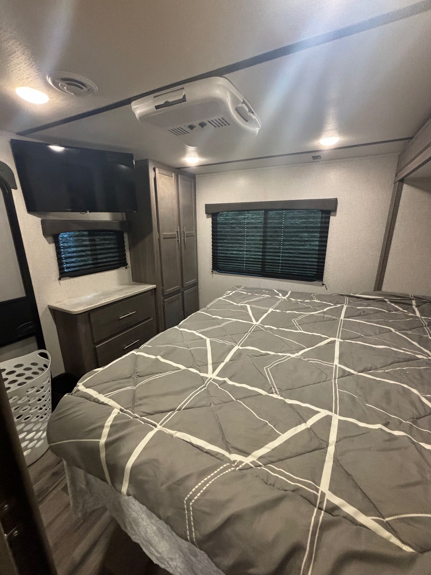 Compact RV rental bedroom featuring a grey bed, wall-mounted TV, storage cabinets, and window blinds.. Crossroads RV Volante 2022