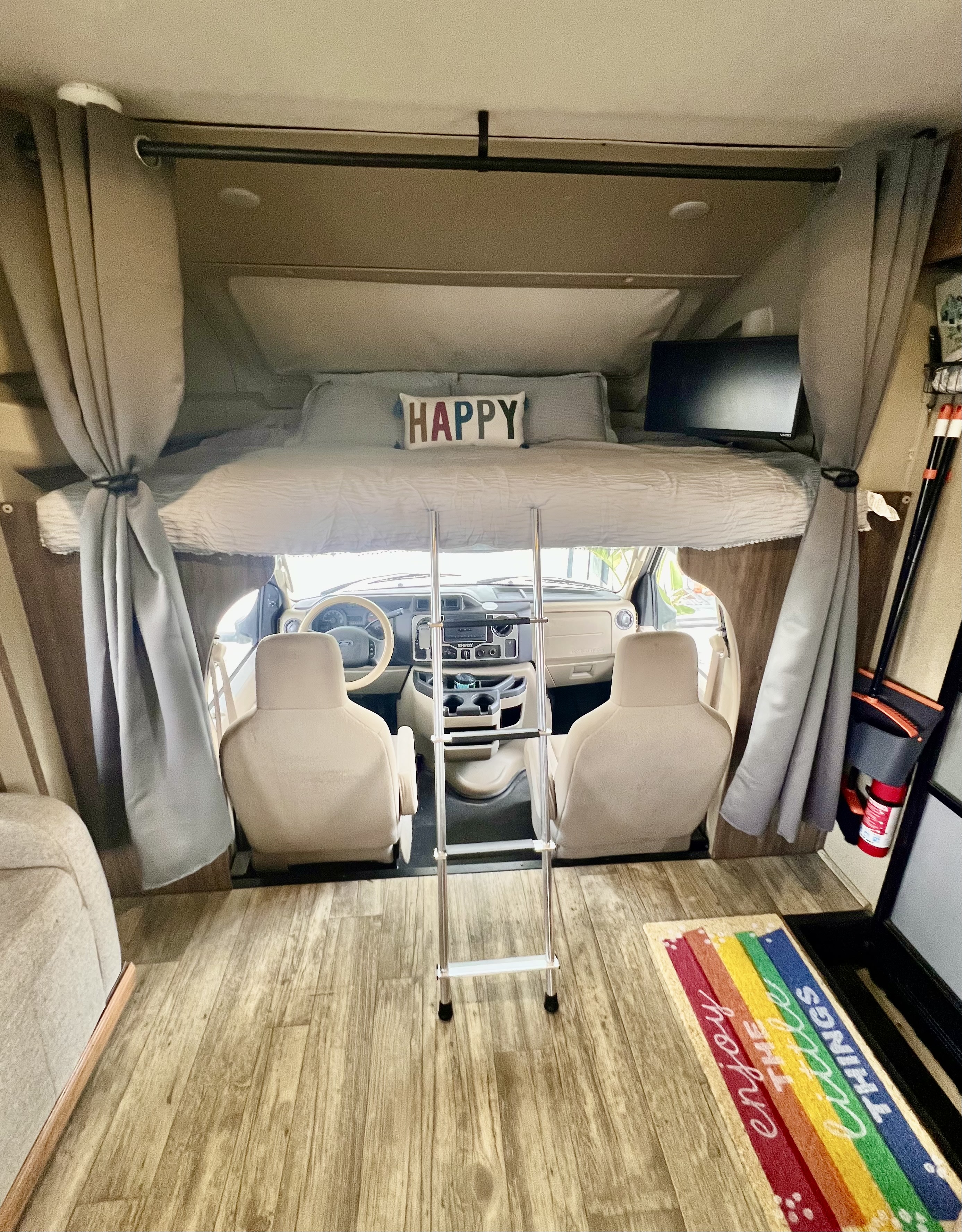 Cozy RV rental interior featuring an over-cab bunk bed, ladder, and bright front cabin view.. Jayco Envoy 100 2018