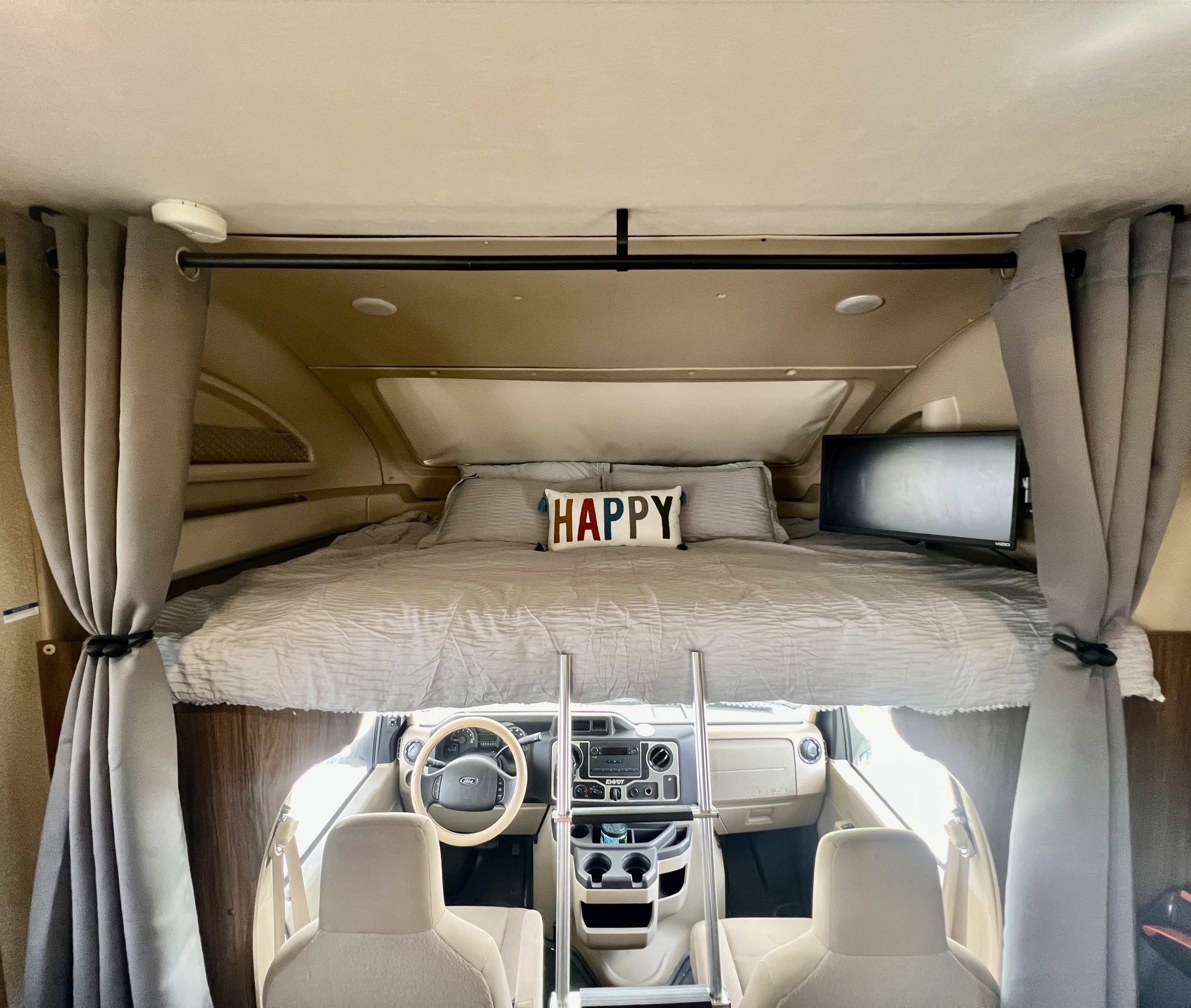 Spacious RV rental interior with a comfy cab-over bunk bed, TV, and Ford cockpit below.. Jayco Envoy 100 2018