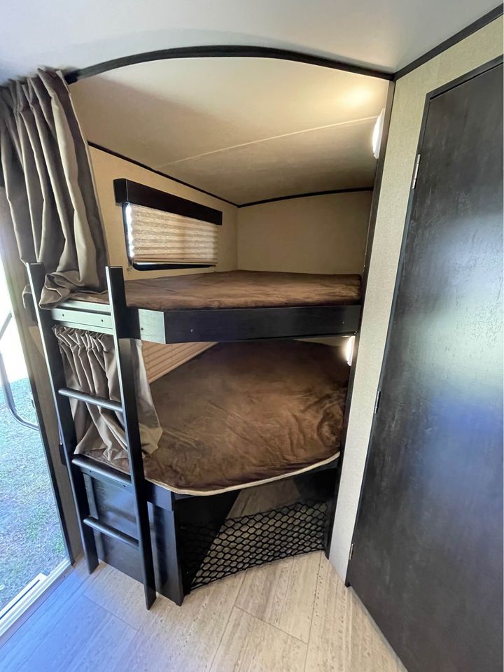 Inside an RV rental: view of cozy bunk beds, ladder, window, and storage net below.. Grand Design Imagine 2017