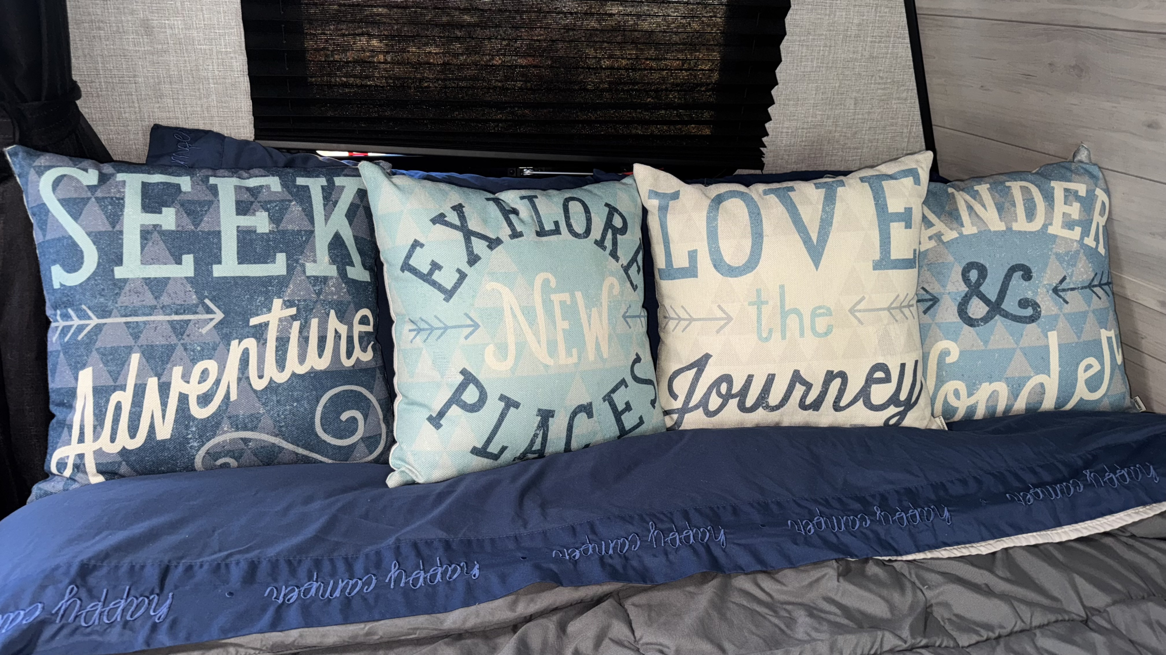 Cozy RV rental bed with adventure-themed pillows ("Seek Adventure," "Explore New Places") and a "happy camper" blanket.. Jayco Jay Flight SLX 2022