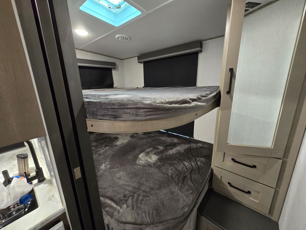 Inside this RV rental, find comfortable bunk beds with grey bedding and handy storage next to a sink area. Perfect for families.. Grand Design Reflection 150 2023