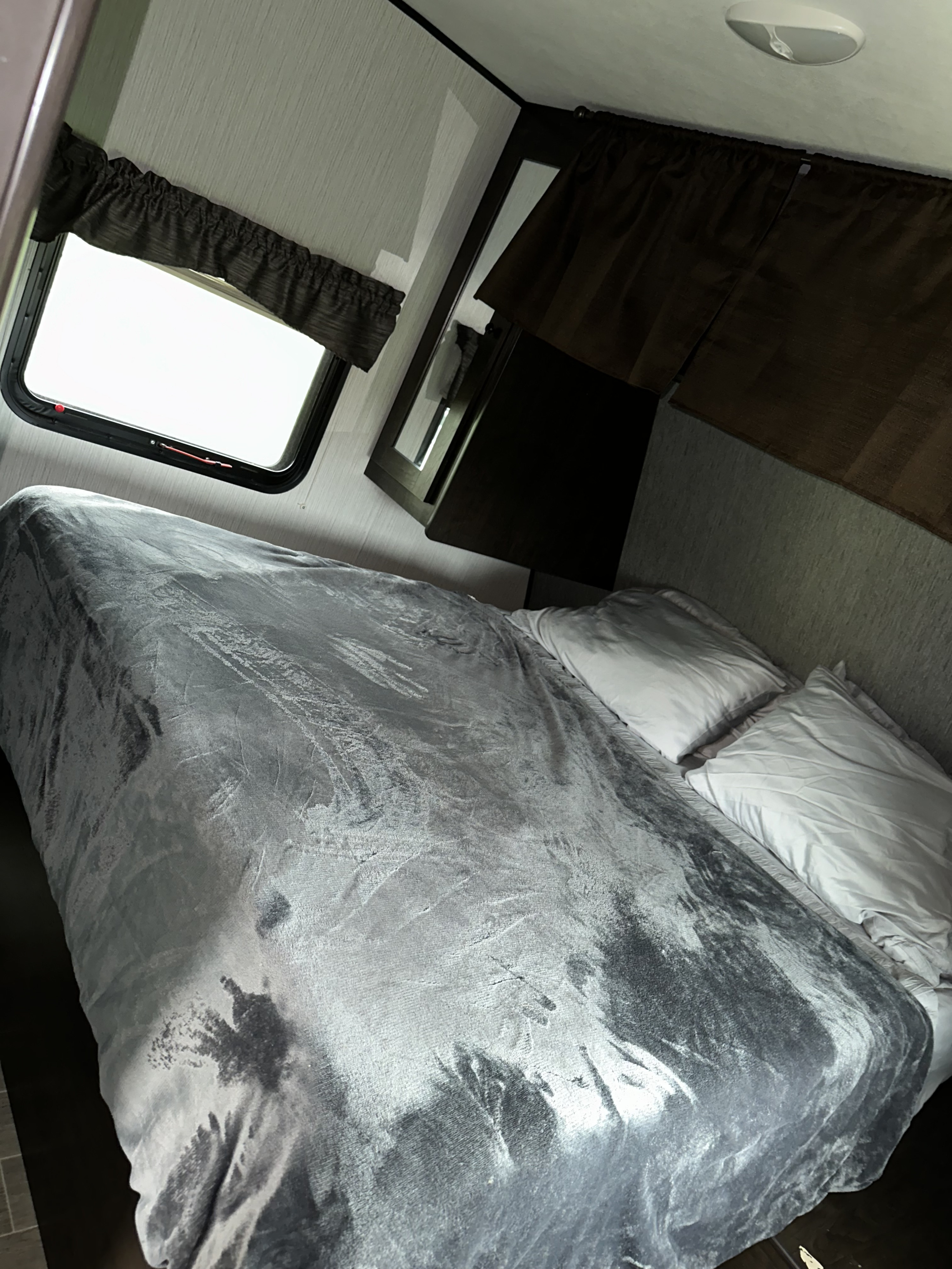 Explore this comfortable RV rental bedroom, featuring a plush gray blanket, white pillows, and side window.. Heartland RVs Trail Runner 2020