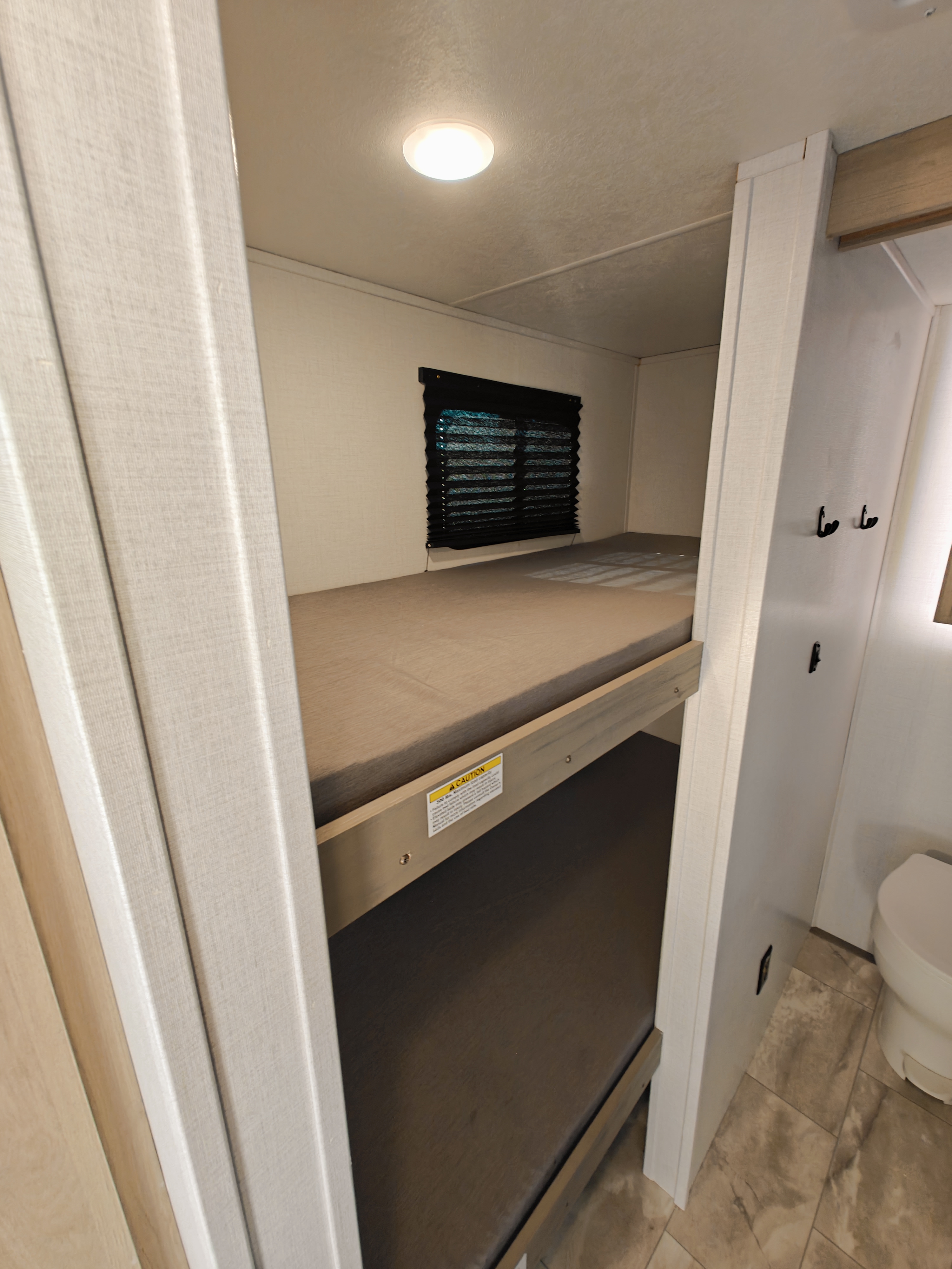 Experience comfort in this RV rental's bunk bed area, featuring a window, ceiling light, and nearby bathroom with toilet and hooks.. Dutchmen Kodiak Cub 170BH 2025