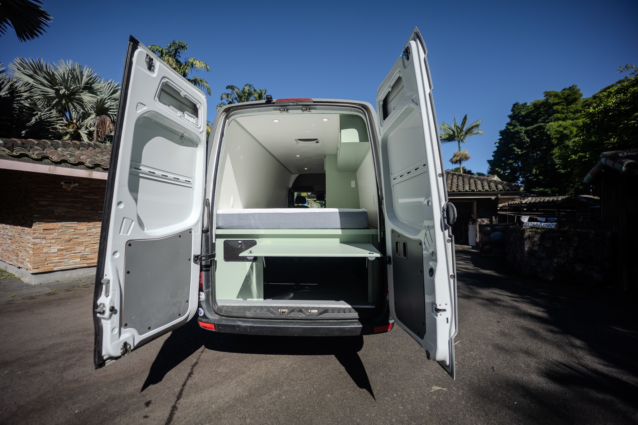 RV rental: Bright custom camper van interior visible from open rear doors, featuring a bed and storage.. Mercedes-Benz Sprinter 419 LWB High Roof 2013