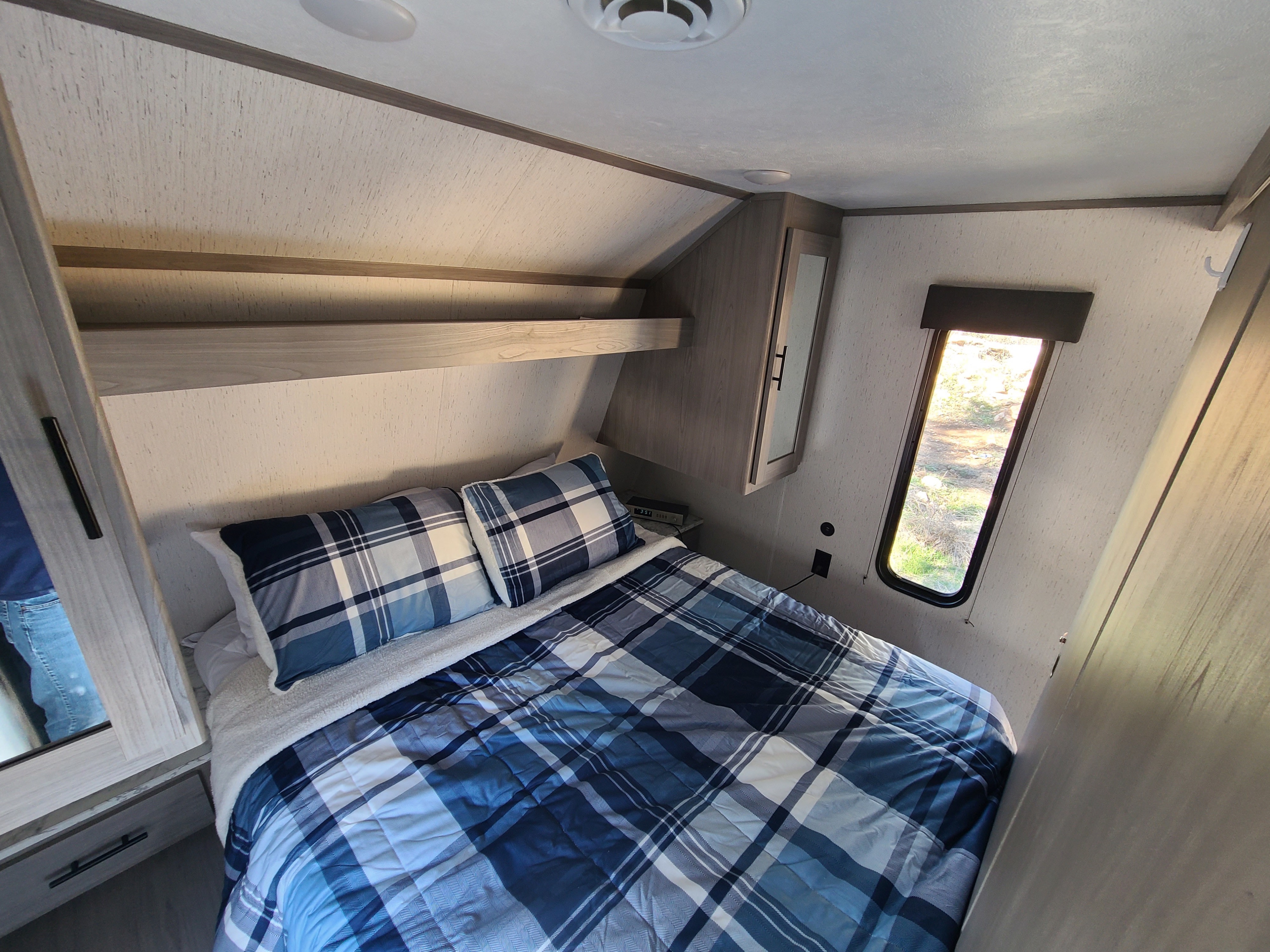 An inviting RV rental bedroom with a plaid bed, ample storage, and a scenic window view for travel comfort.. Dutchmen Coleman 2022